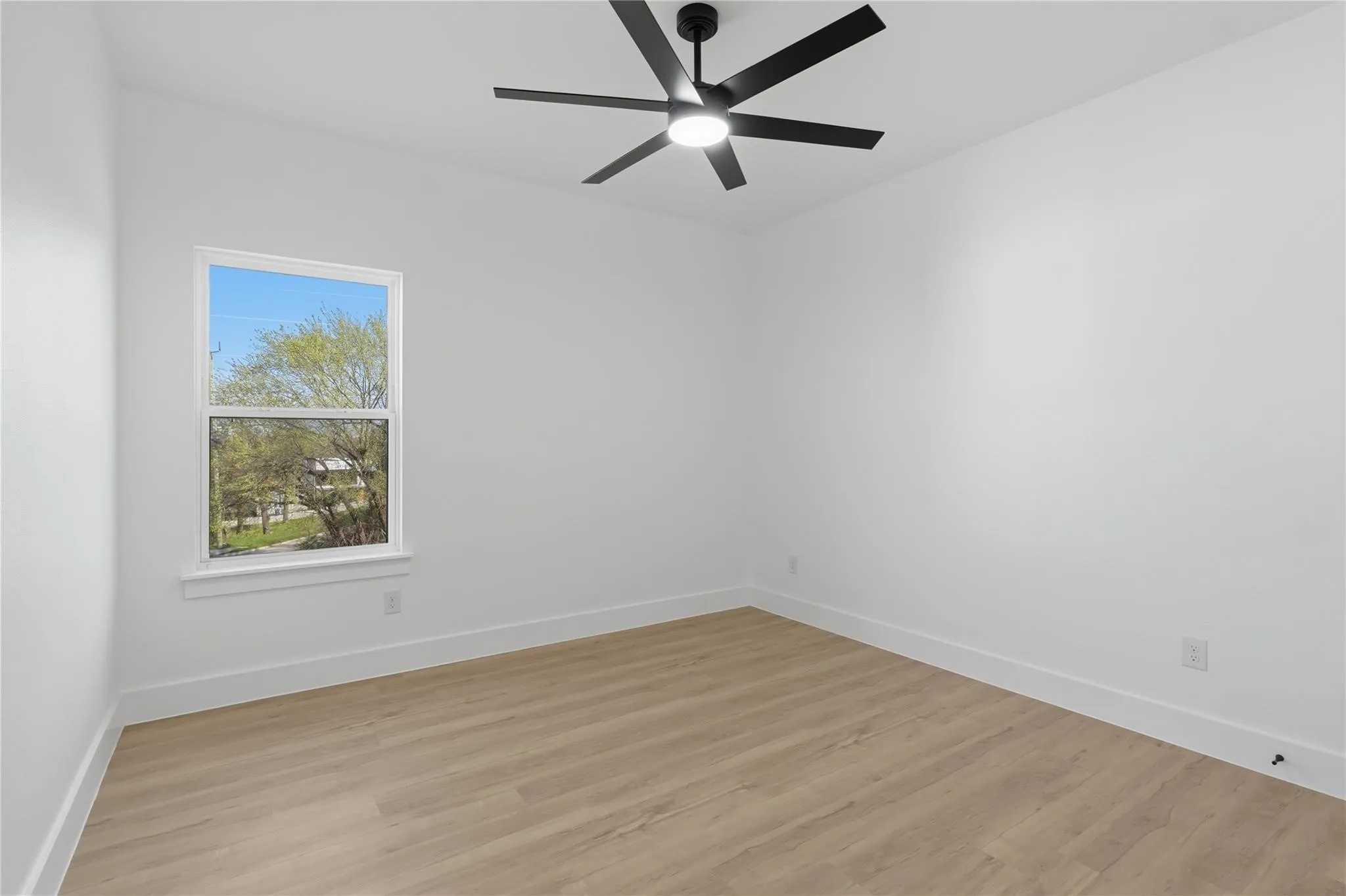 Bright interior room featuring wood-finish flooring, white walls, and a modern ceiling fan with integrated lighting