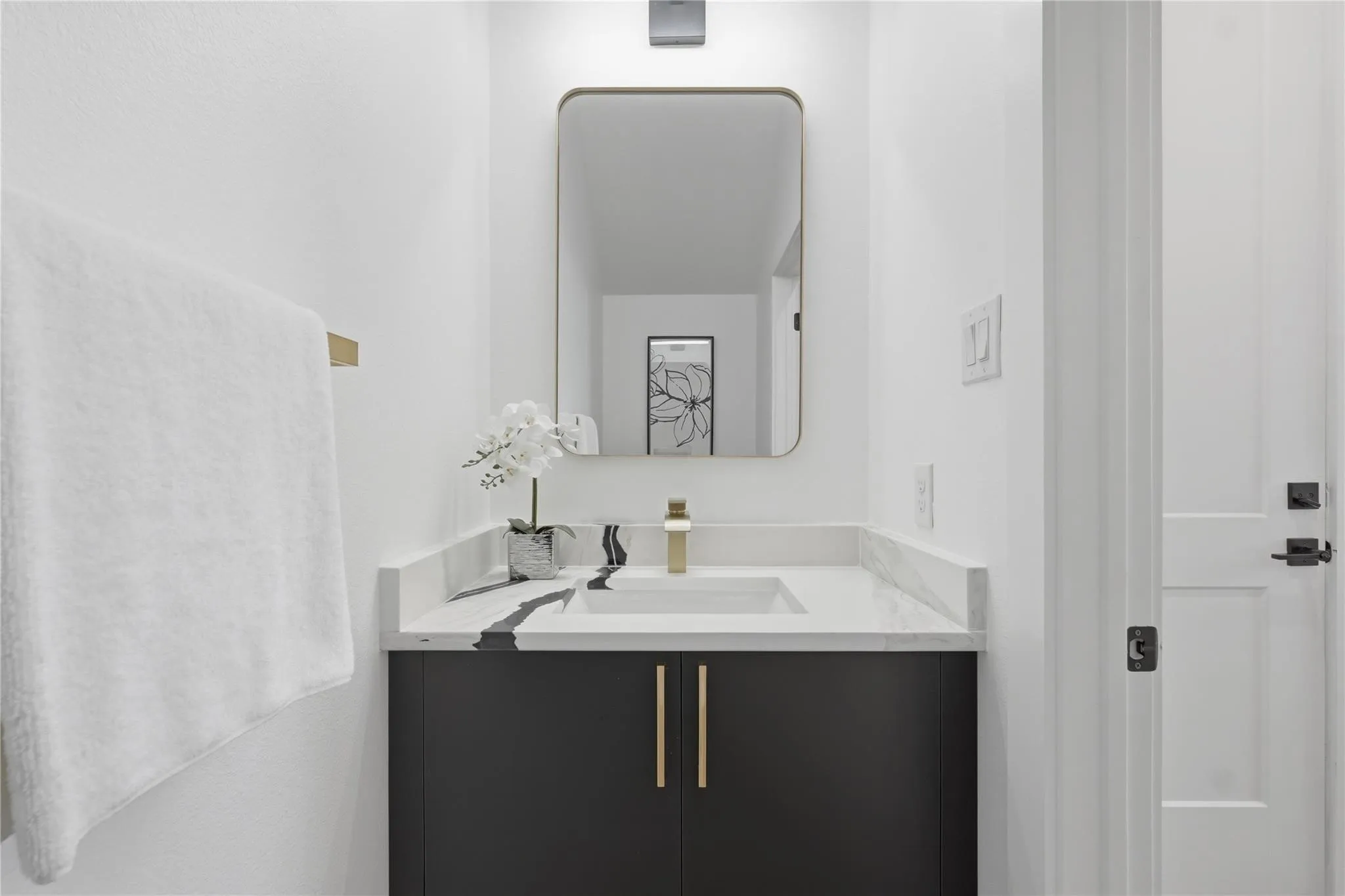 Modern vanity featuring a dark finish cabinet with gold-tone hardware, an integrated rectangular sink, and a white countertop with grey veining