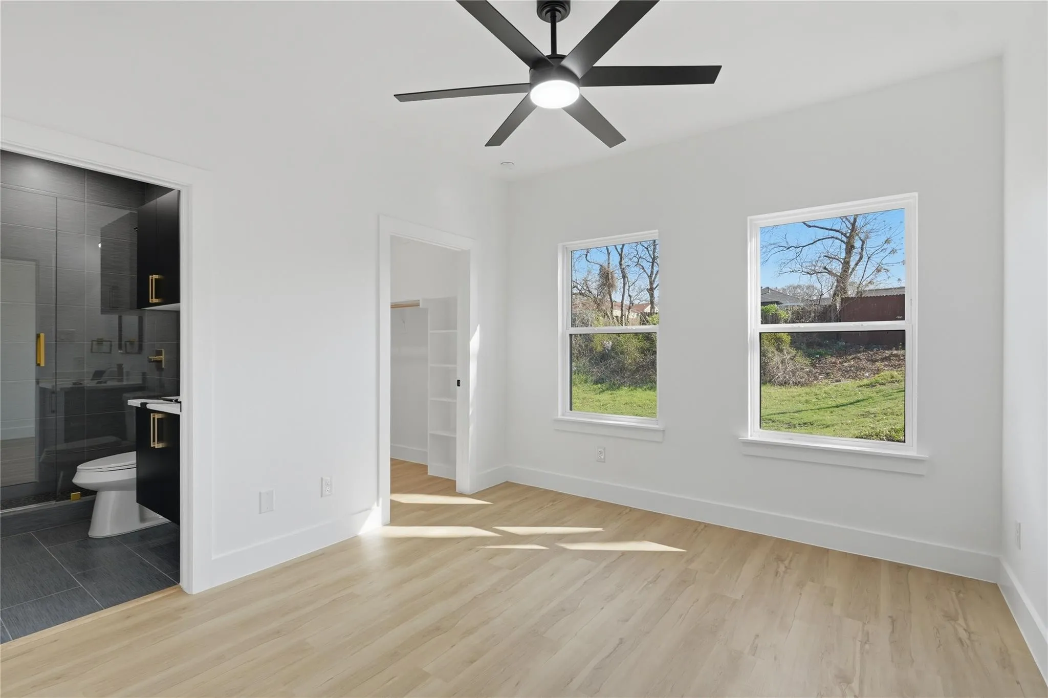 Bright room featuring light wood-finish flooring, a modern black ceiling fan, and two large windows