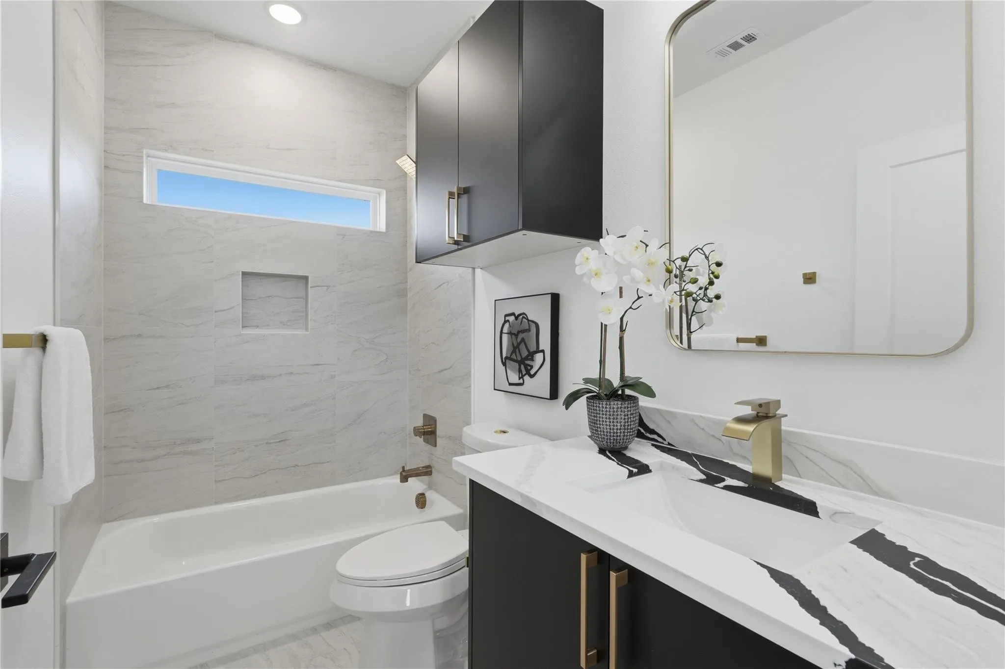 Modern bathroom featuring a vanity with a white countertop displaying dramatic black veining, a gold-toned faucet, and dark cabinetry with gold-toned hardware