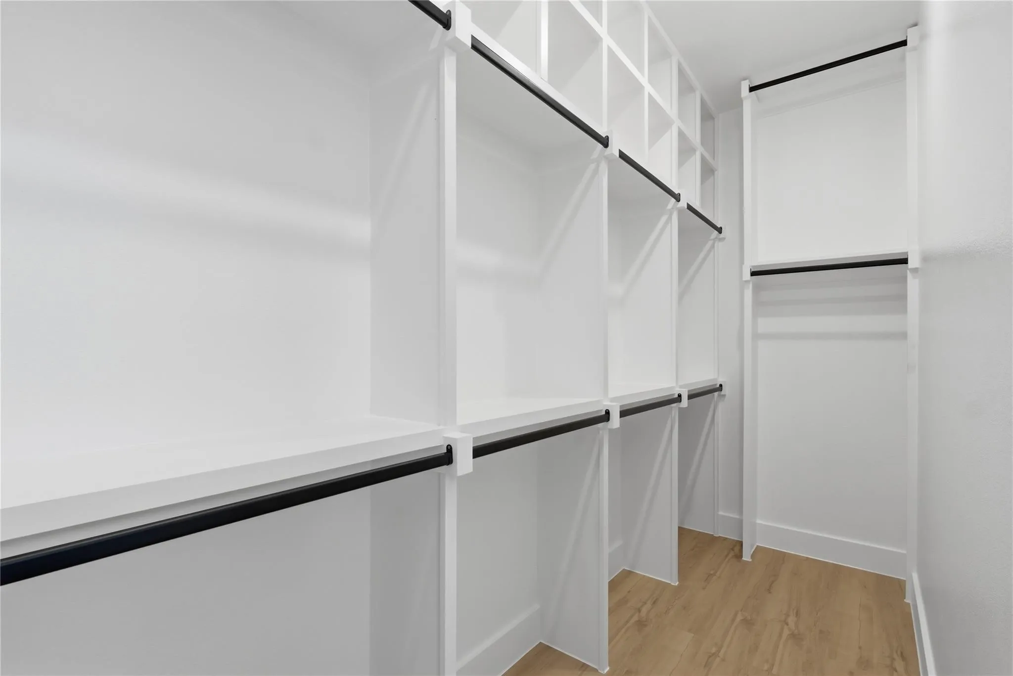 Custom closet system featuring white shelving units, multiple hanging rods, integrated cubby storage, and wood-finish flooring