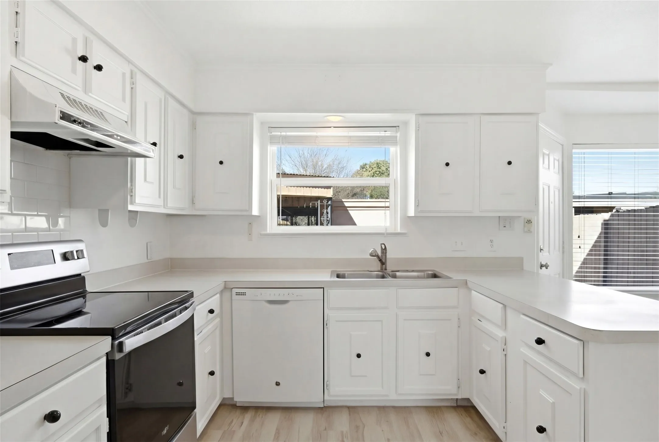 U-shaped kitchen featuring white cabinetry, light-toned countertops, subway tile backsplash, and wood-finish flooring
