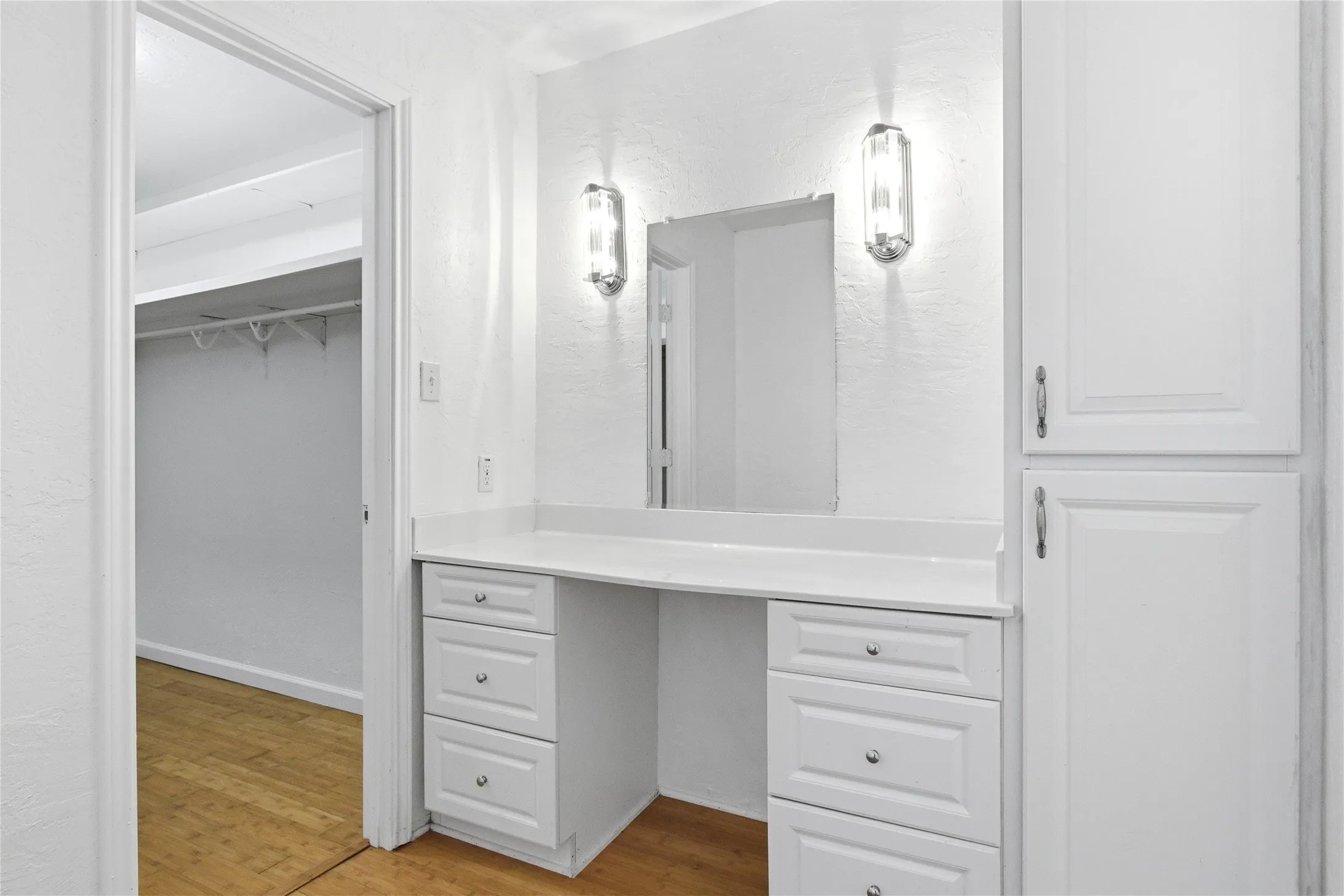 Built-in vanity with a solid surface countertop, integrated mirror, and sconce lighting