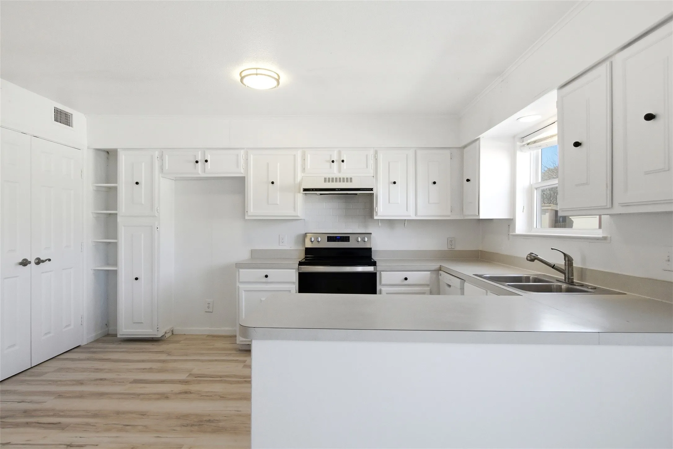 Contemporary kitchen featuring white cabinetry, light-toned countertops, a stainless steel electric range, and wood-finish flooring
