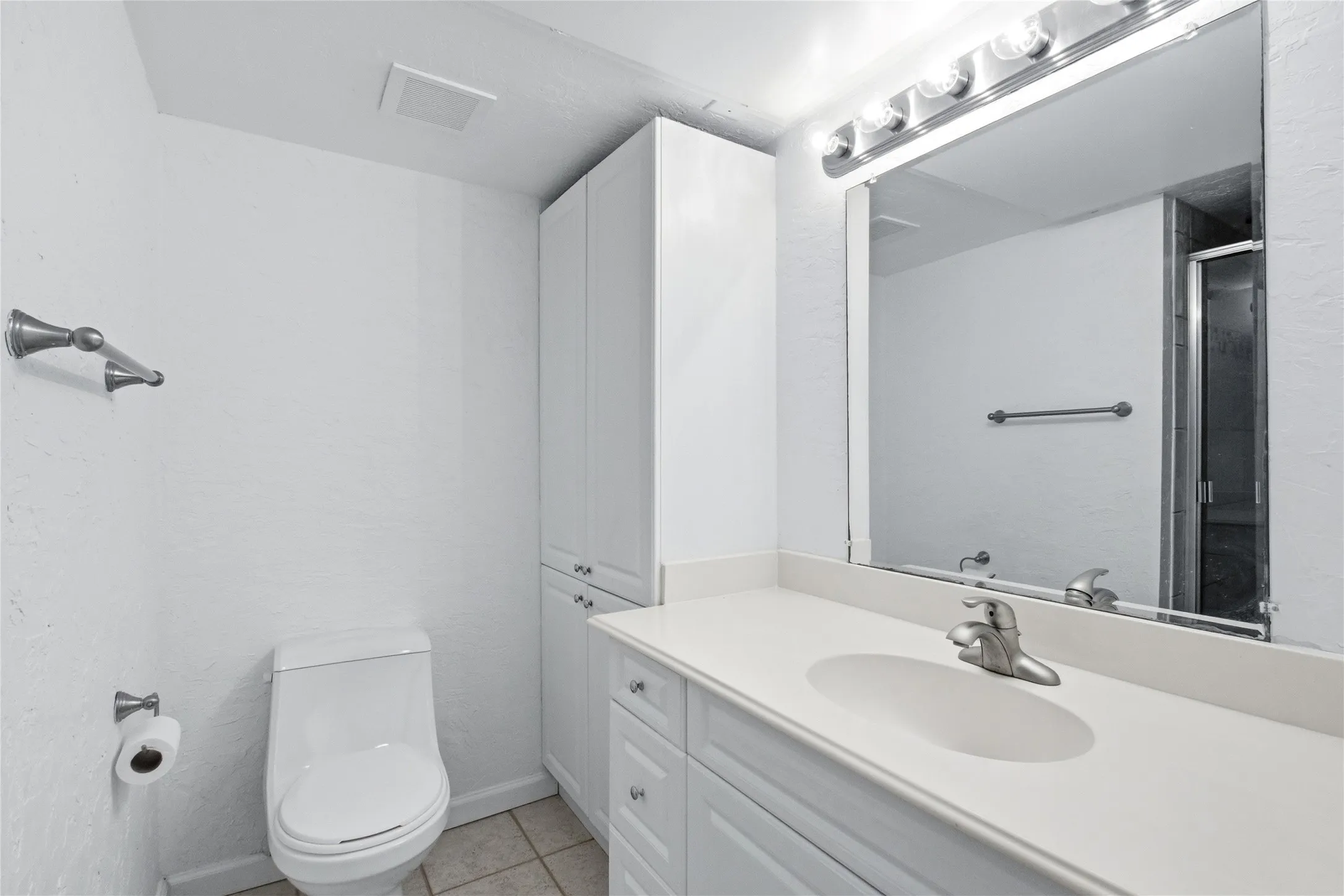 Bathroom featuring a single vanity with an integrated sink, brushed nickel faucet, large mirror, white cabinetry, and a stand-alone shower with a glass enclosure