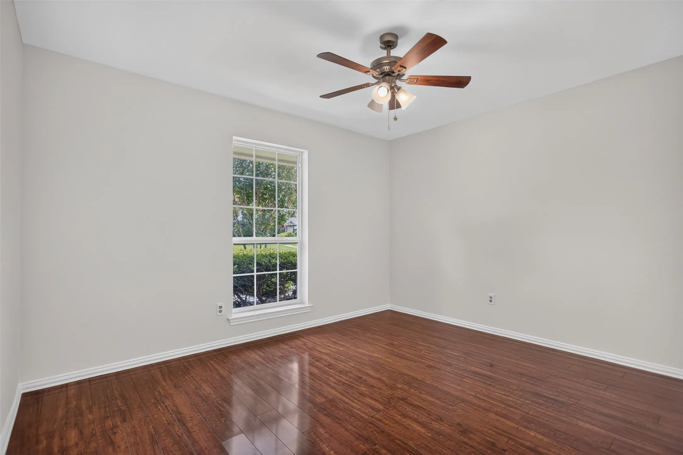 Spacious room featuring wood-finish flooring, light neutral wall tones, and a window with white trim