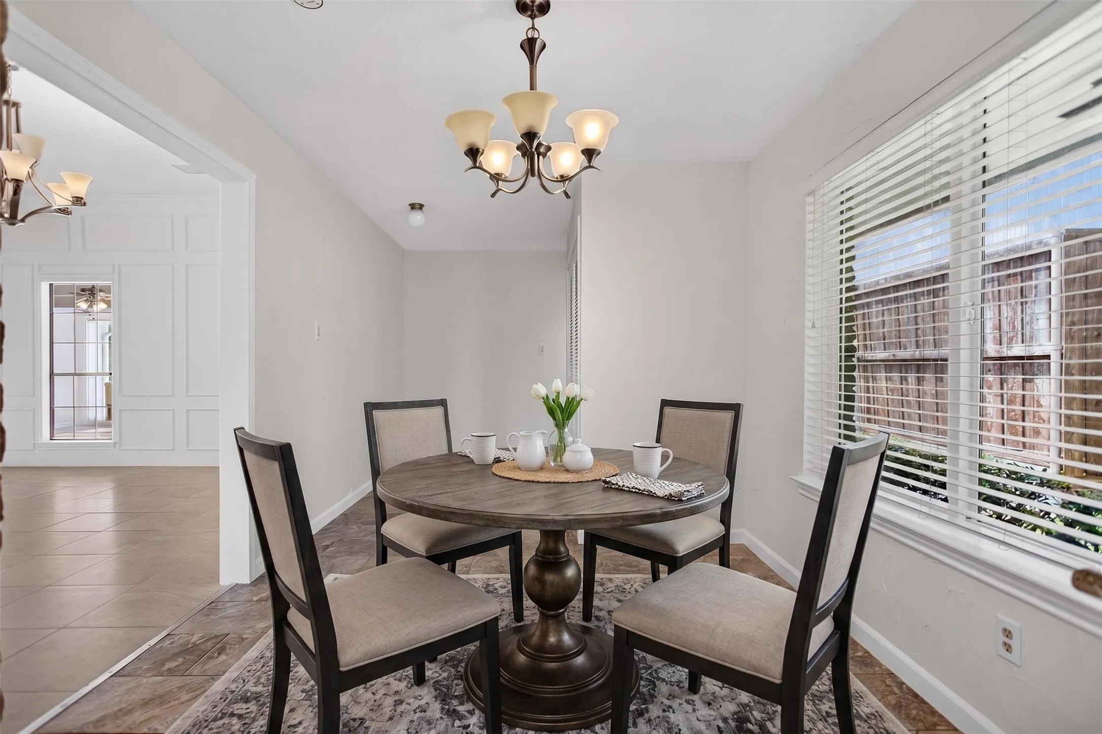 Dining area featuring a bronze chandelier with frosted glass shades, a window with blinds, and tile flooring