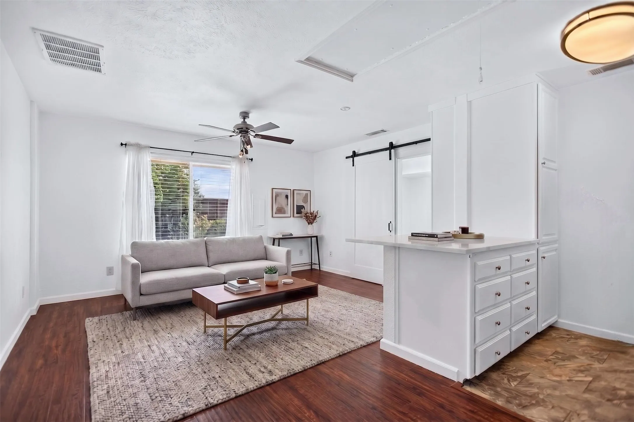 Open-concept living space featuring wood-finish flooring, a ceiling fan with integrated lighting, and a window with blinds