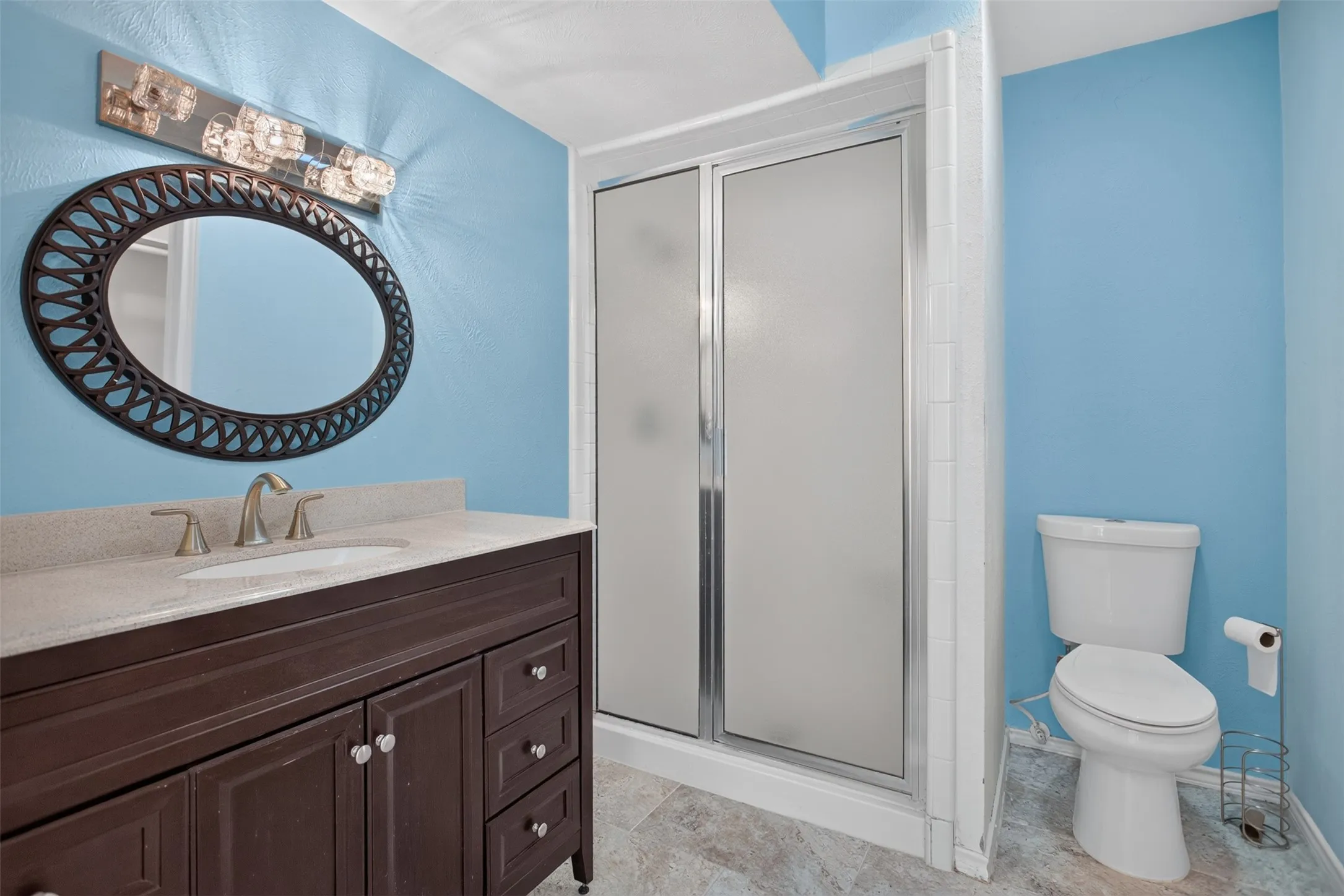 Bathroom featuring a dark wood finish vanity with a light-toned countertop, oval mirror, and a modern light fixture
