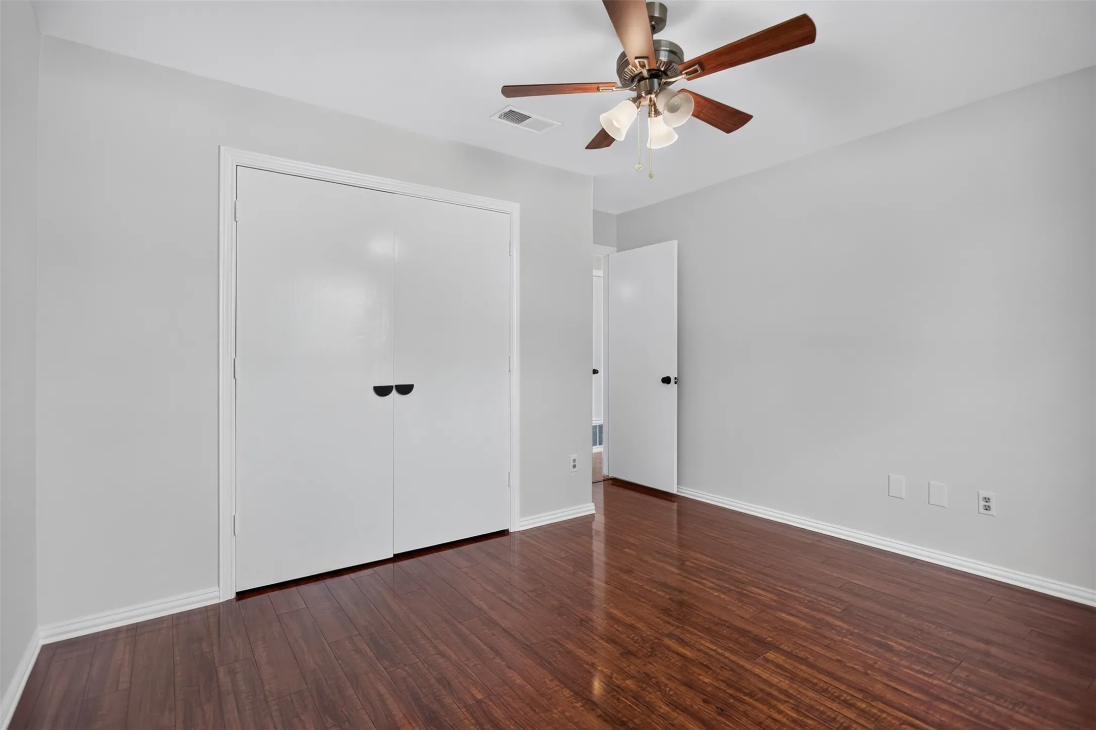 Spacious room featuring wood-finish flooring, light gray walls, white trim, and a ceiling fan with integrated lighting