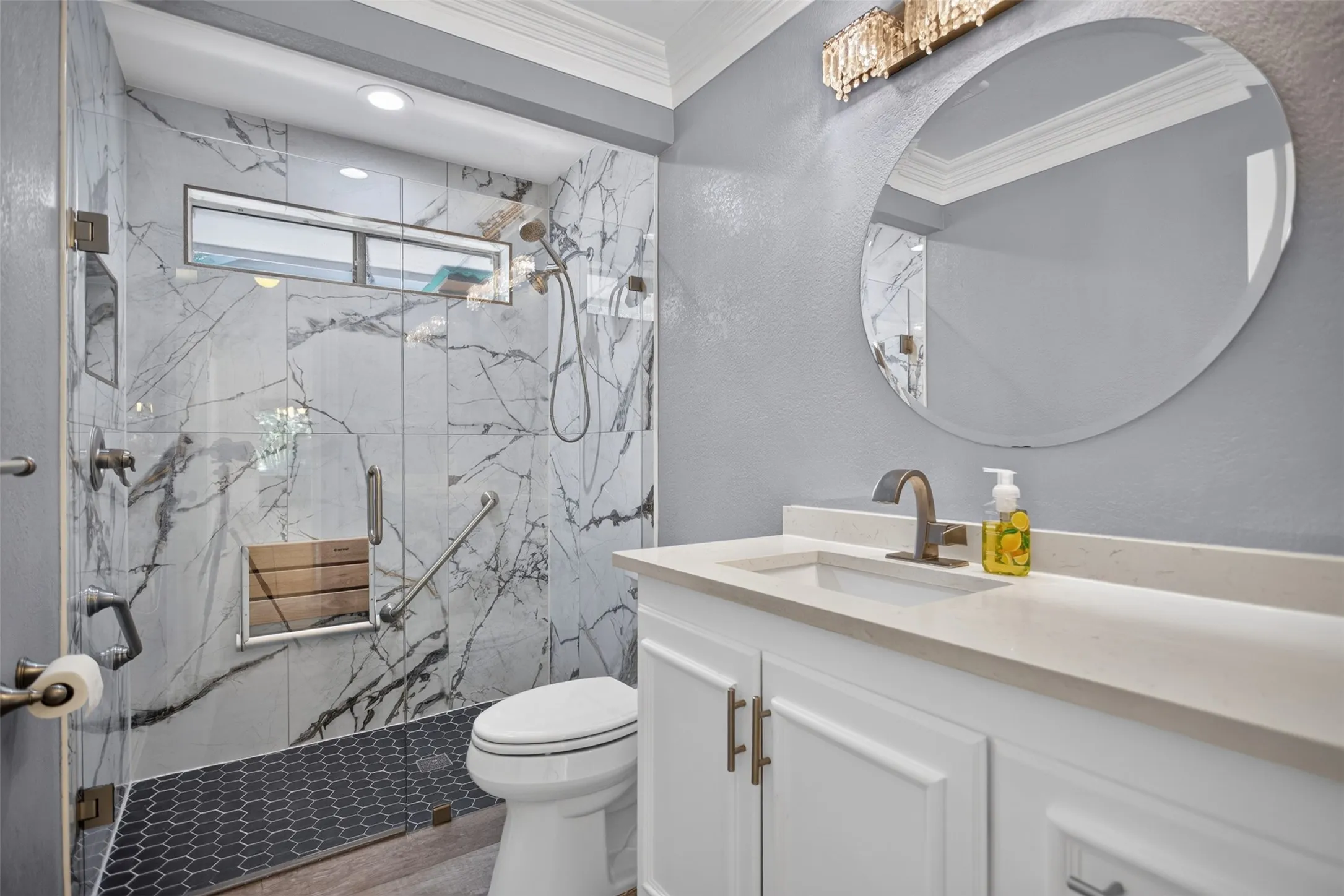 Walk-in shower featuring large format marble-look tile, dark hexagonal floor tiling, a frosted transom window, and an integrated wood-slat bench
