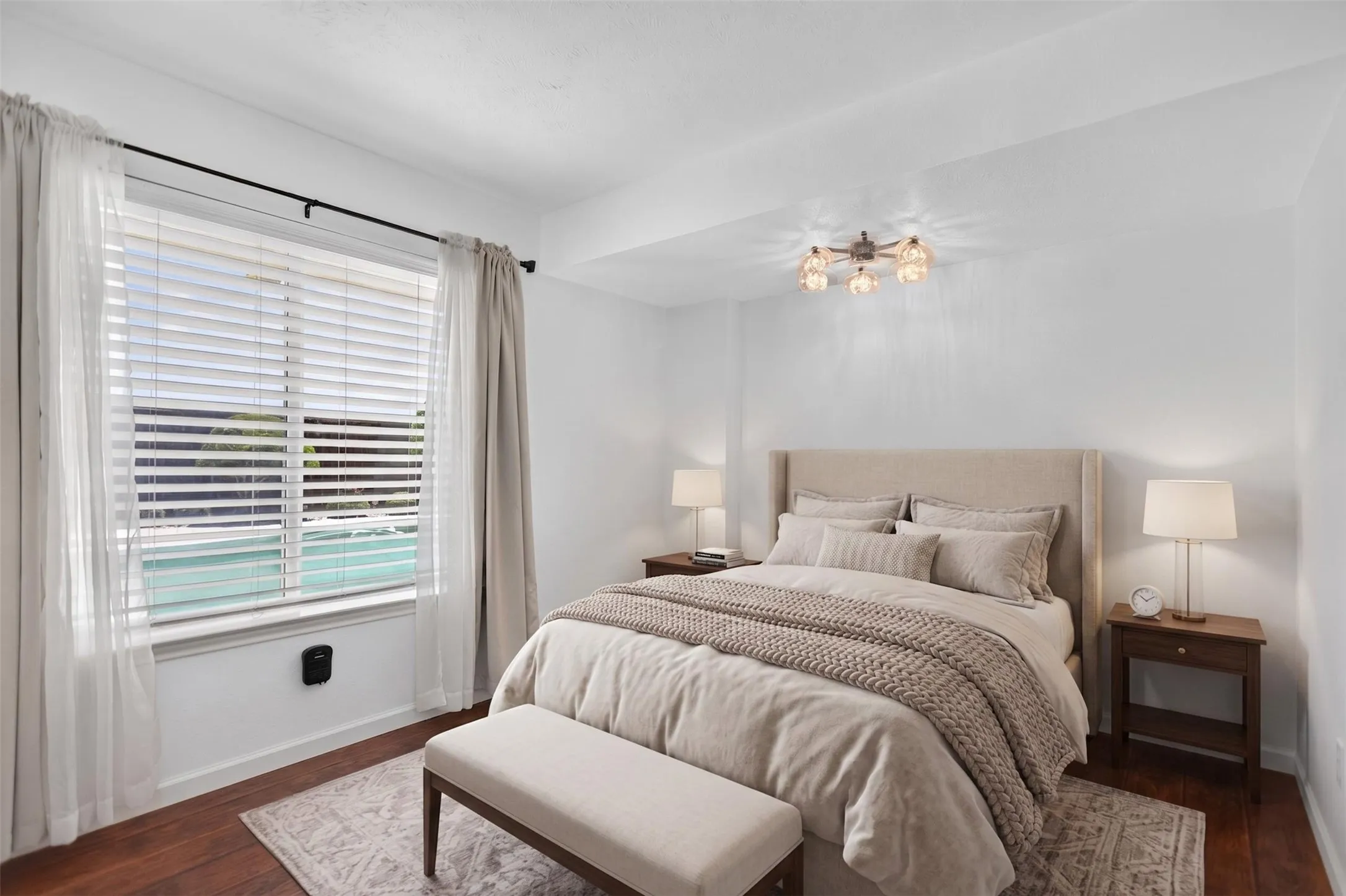Spacious room featuring wood-finish flooring, a large window with horizontal blinds, sheer and opaque drapes on a black rod, and a multi-bulb ceiling fixture