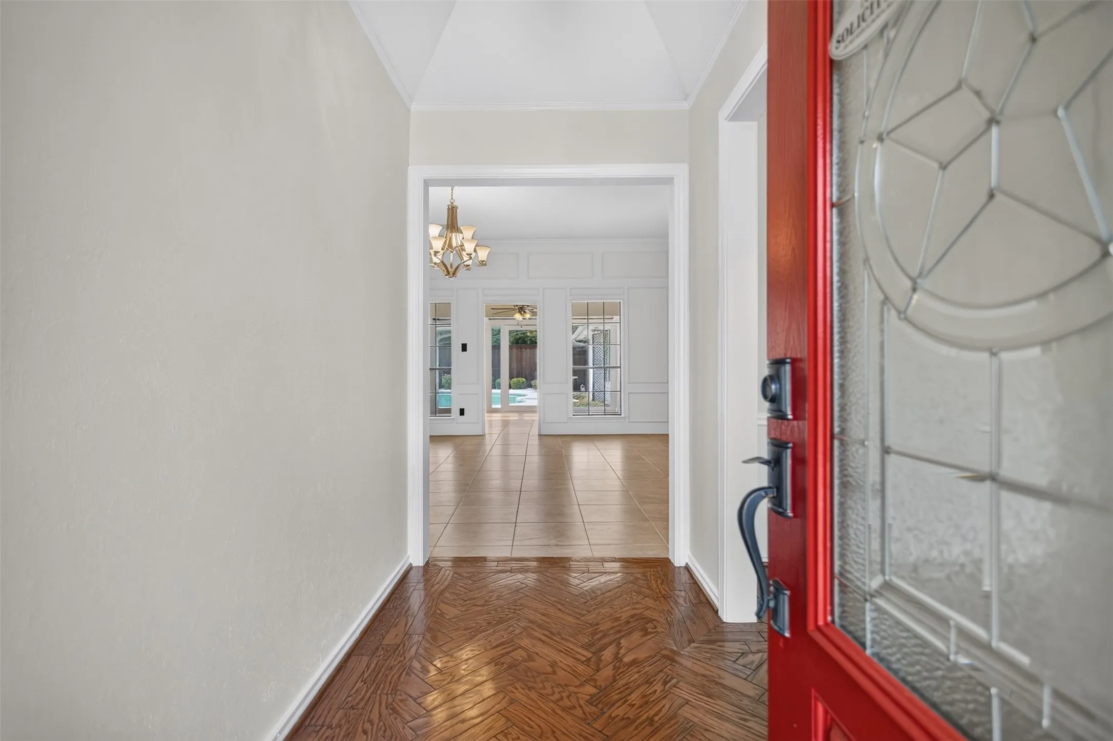 Entryway featuring a red front door with leaded glass, herringbone wood-finish flooring, and a glimpse of an interior chandelier