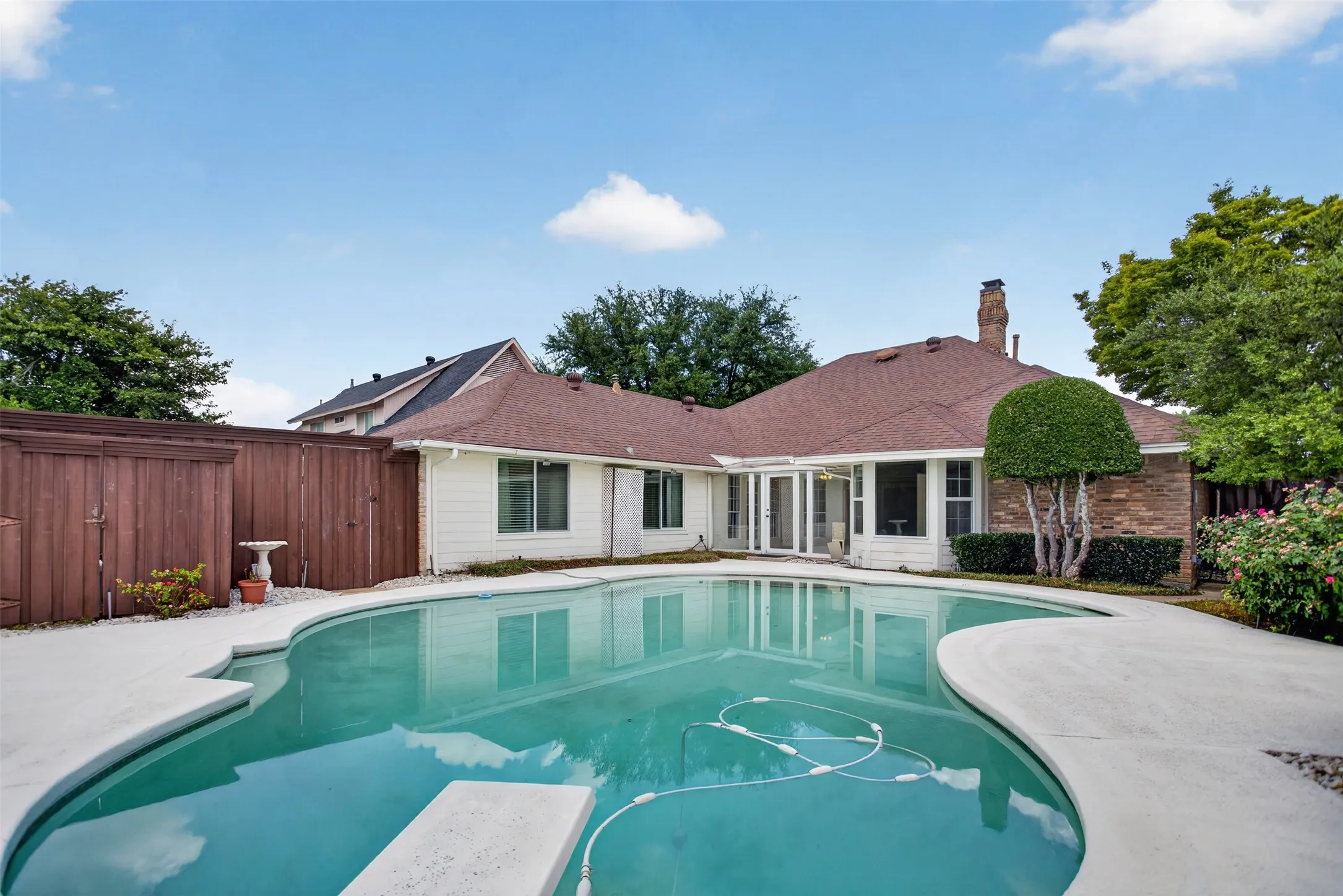 Backyard oasis featuring a curvilinear swimming pool with concrete decking