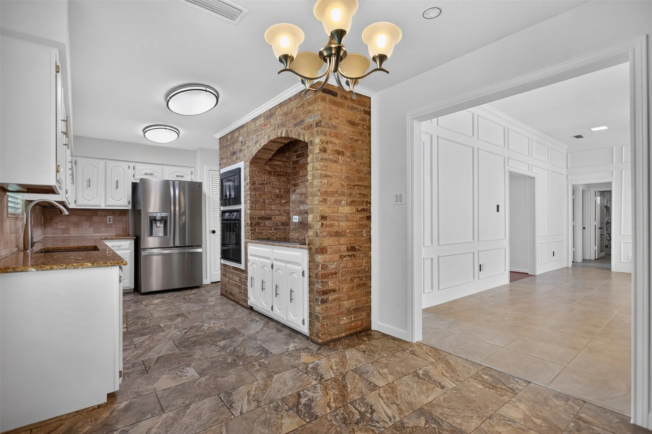 Kitchen featuring brick archway, white cabinetry, stainless steel refrigerator, granite countertops, and tile flooring