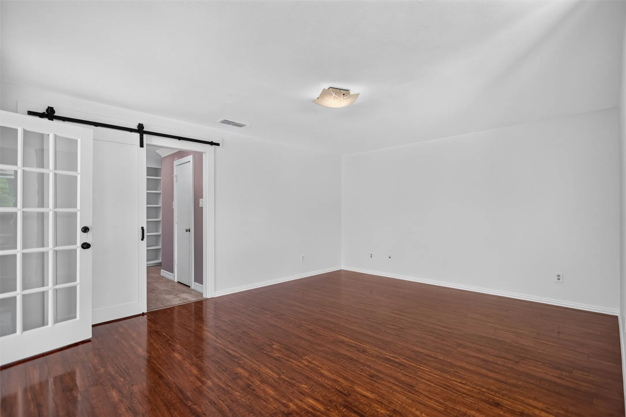 Spacious room featuring wood-finish flooring, white walls, and a ceiling-mounted light fixture
