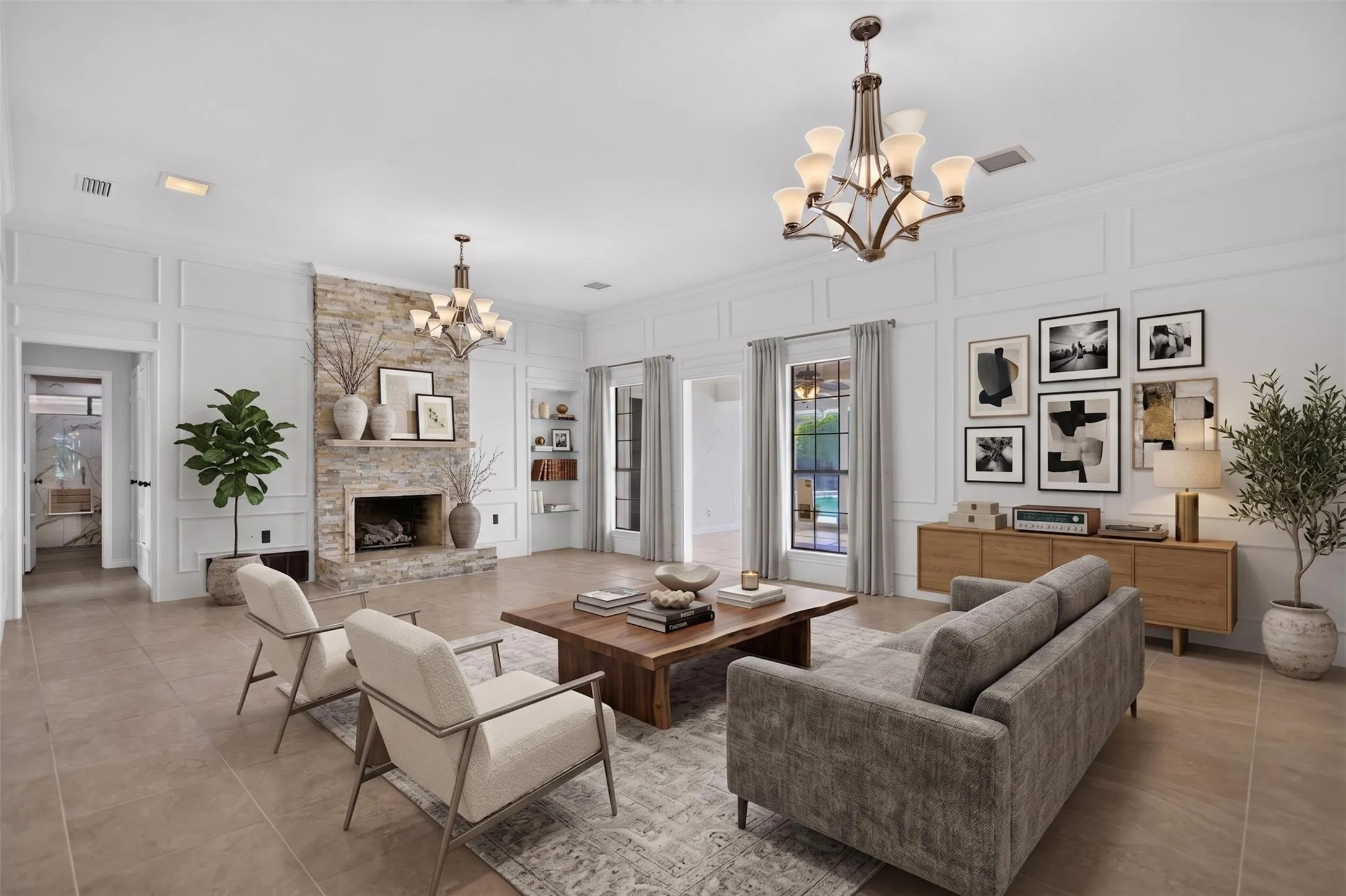 Spacious living area featuring a stone-clad fireplace, tile flooring, two multi-arm chandeliers, and panel molding