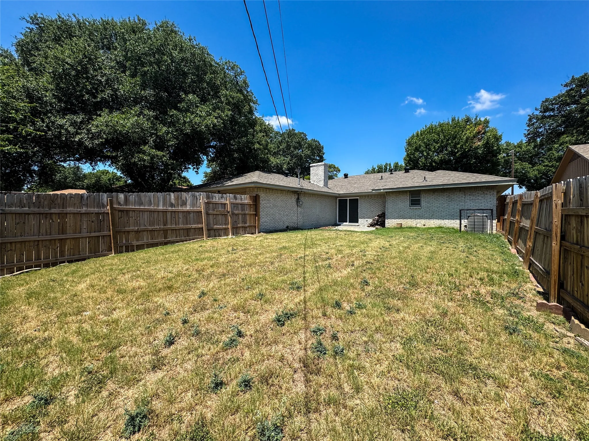 Expansive fenced backyard featuring a concrete patio, brick exterior, and mature trees