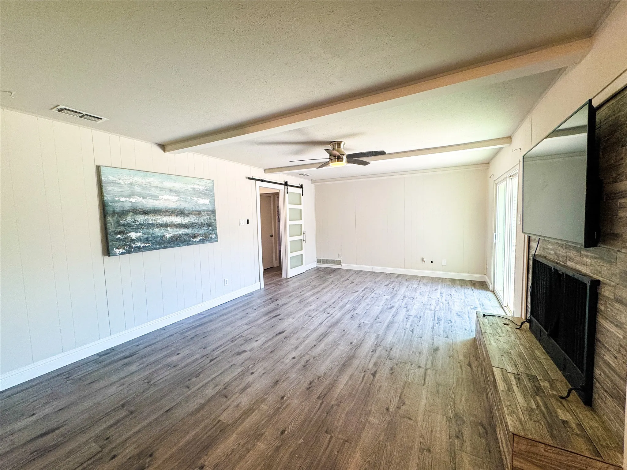 Spacious room featuring wood-finish flooring, a ceiling fan, and exposed ceiling beams