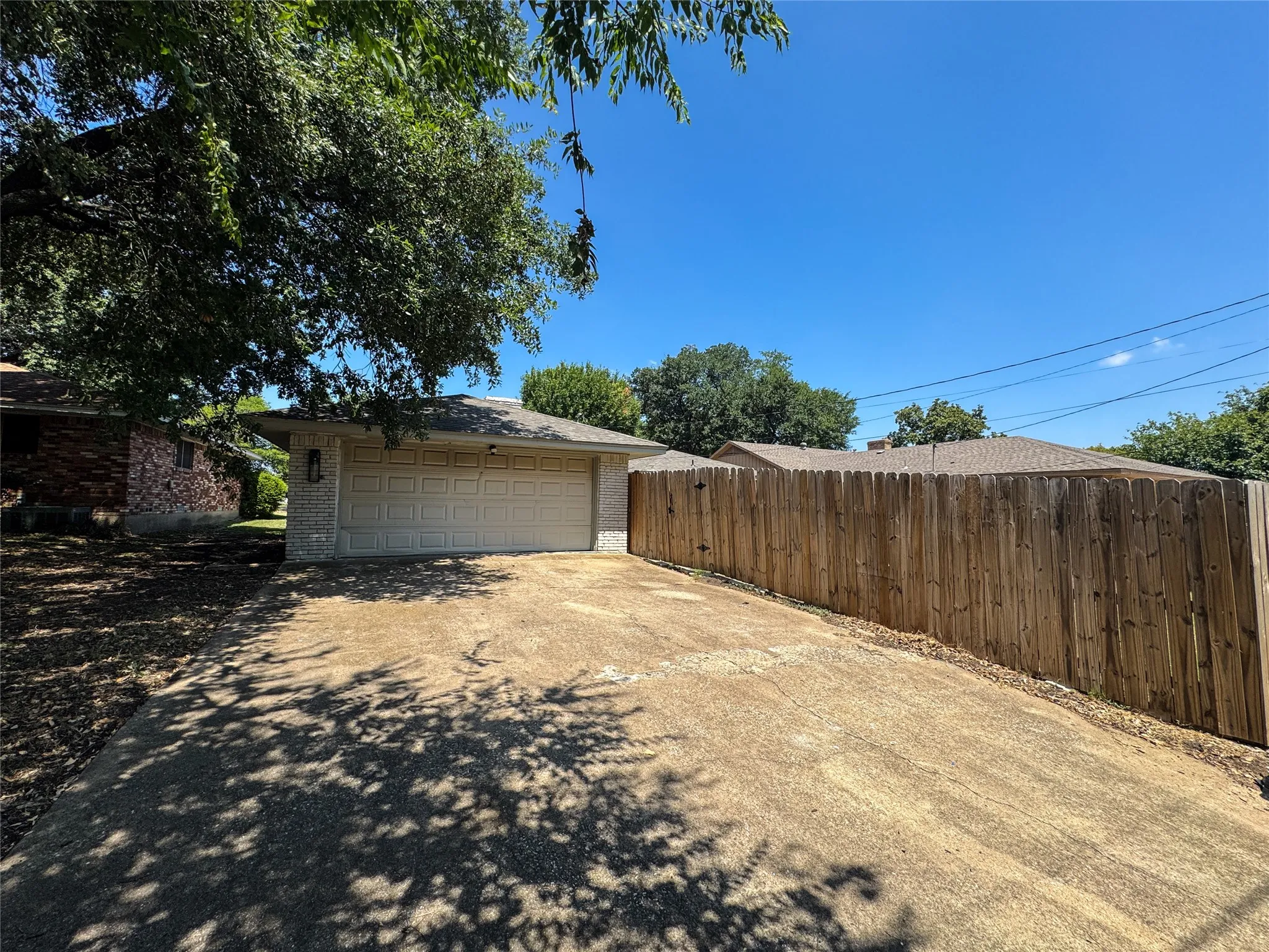 Two-car garage with a textured finish, asphalt shingle roof, and a wood privacy fence