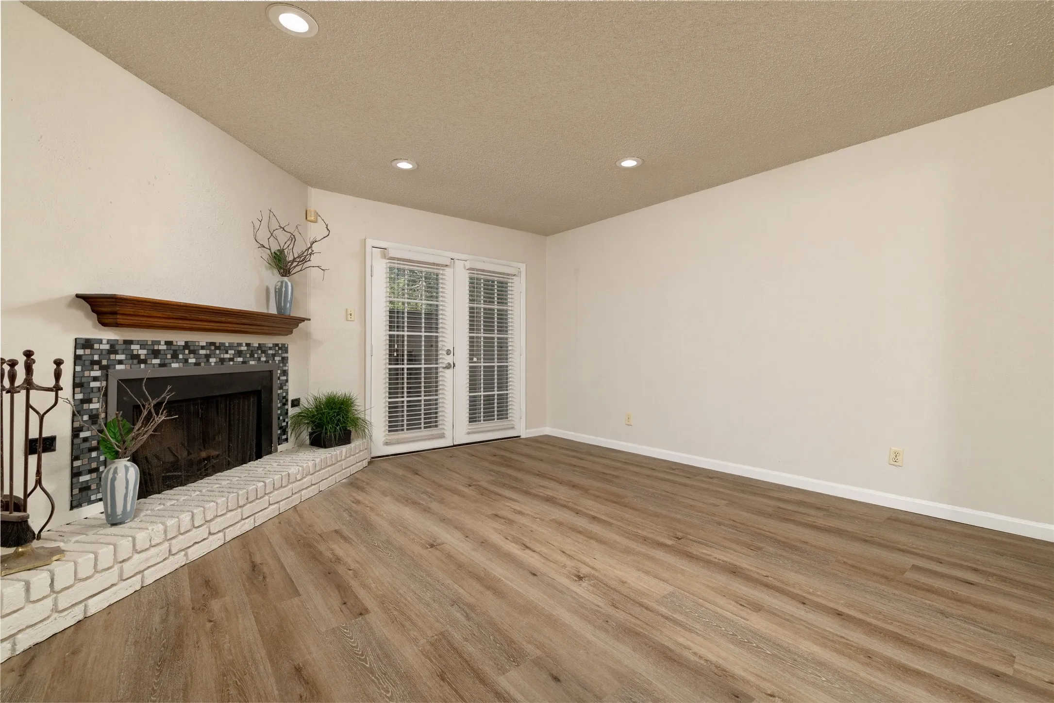 Living area featuring wood-finish flooring, a fireplace with a brick hearth and mosaic tile surround, and recessed ceiling lighting