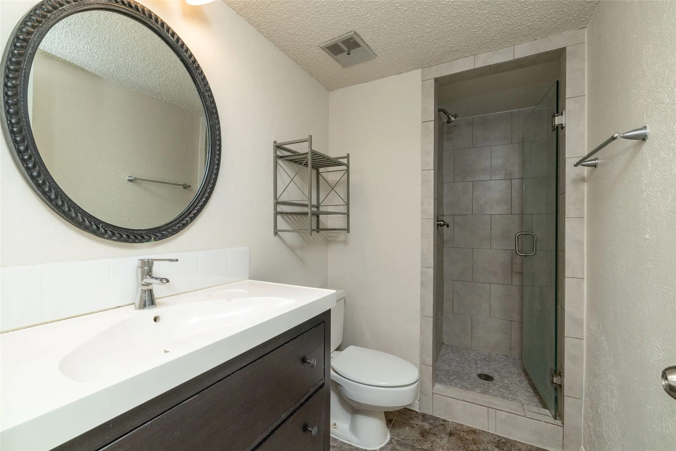 Bathroom featuring a frameless glass shower enclosure, tiled shower surround, and a vanity with an integrated sink
