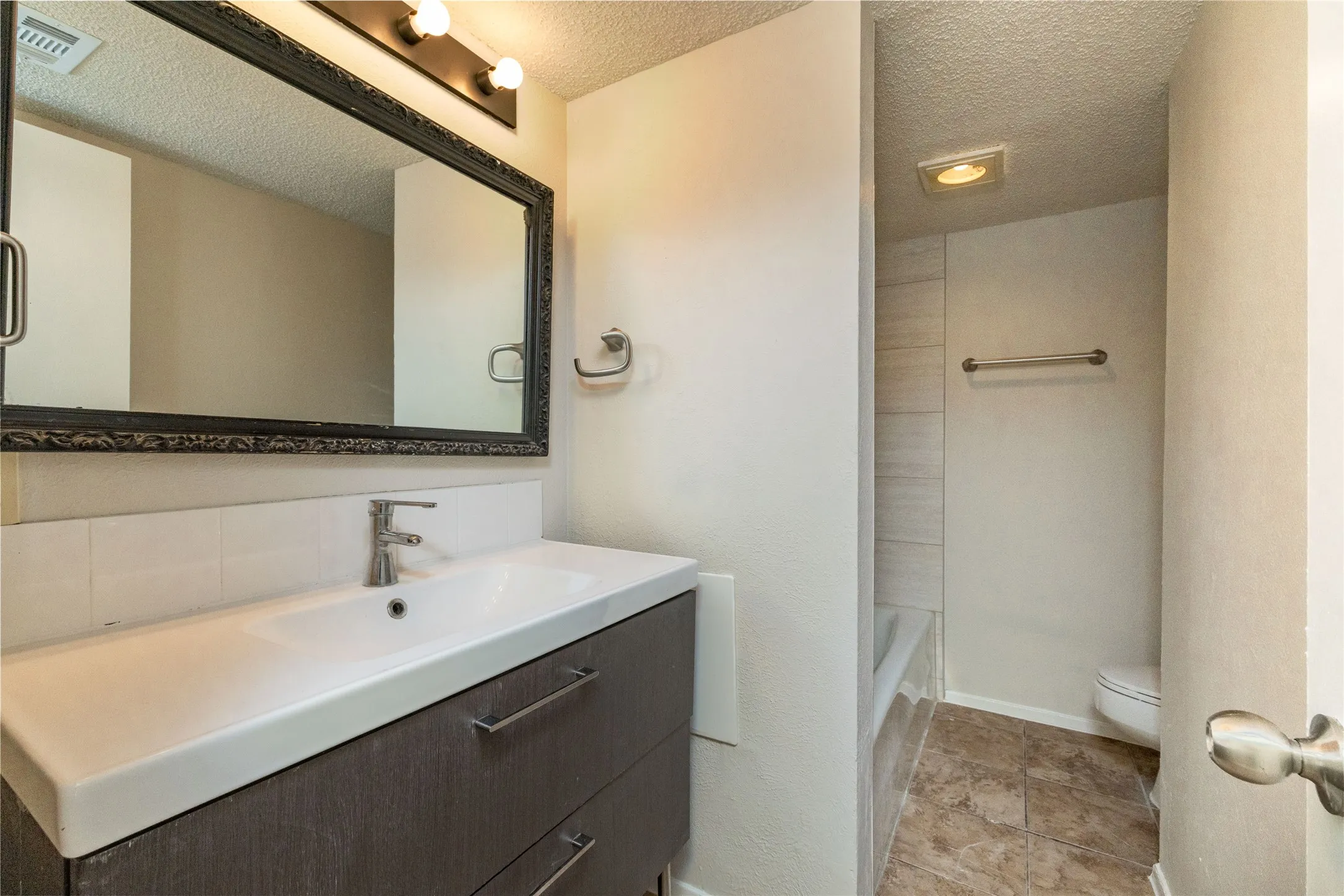 Bathroom vanity featuring a single basin sink, white countertop, and dark wood-finish cabinetry with silver hardware