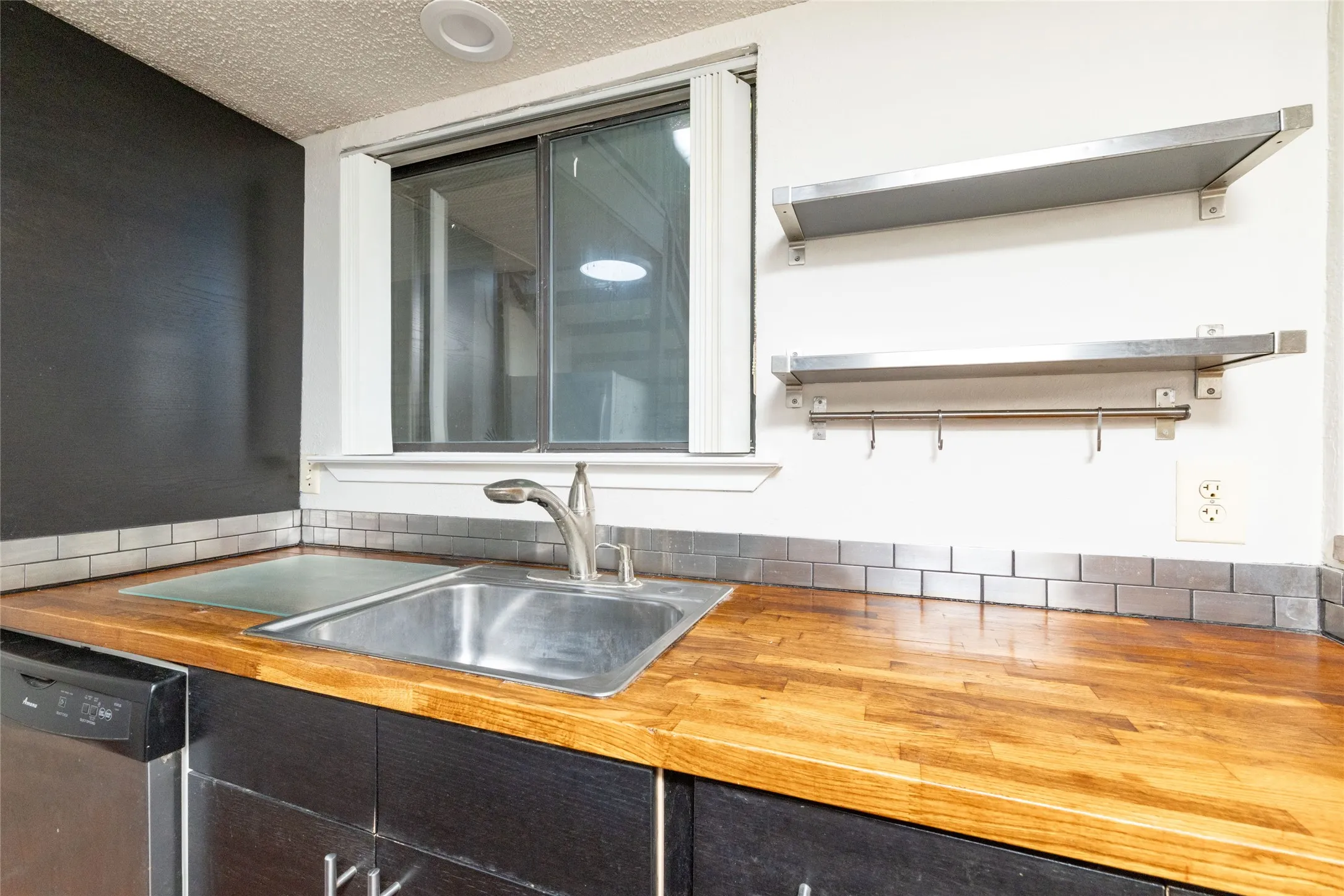 Kitchen workstation featuring a stainless steel sink, wood-finish countertops, subway tile backsplash, and open shelving
