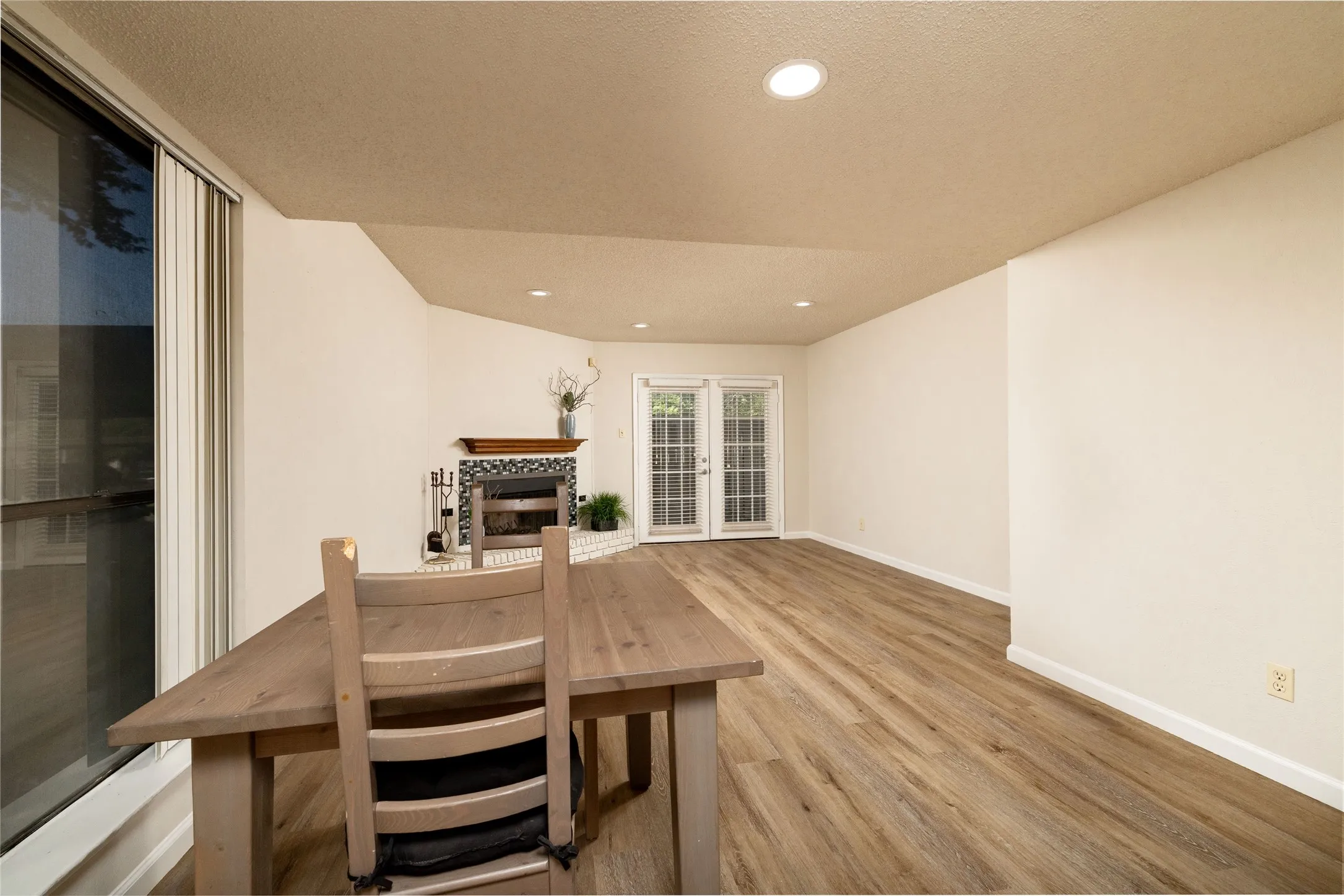Spacious room featuring wood-finish flooring, a decorative fireplace with tile surround, white walls, recessed lighting, and double french doors