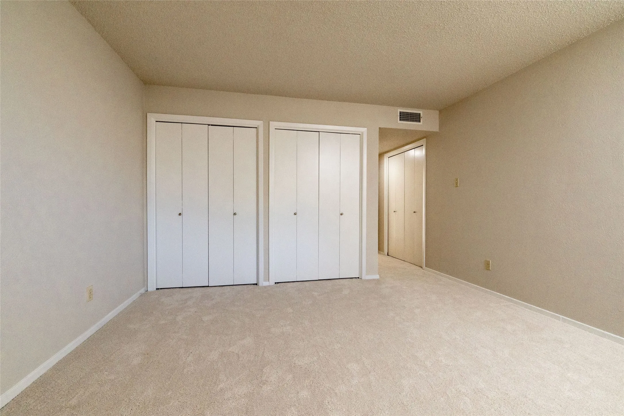 Carpeted interior space featuring two sets of bi-fold closet doors, neutral wall paint, white baseboards, and a ceiling vent