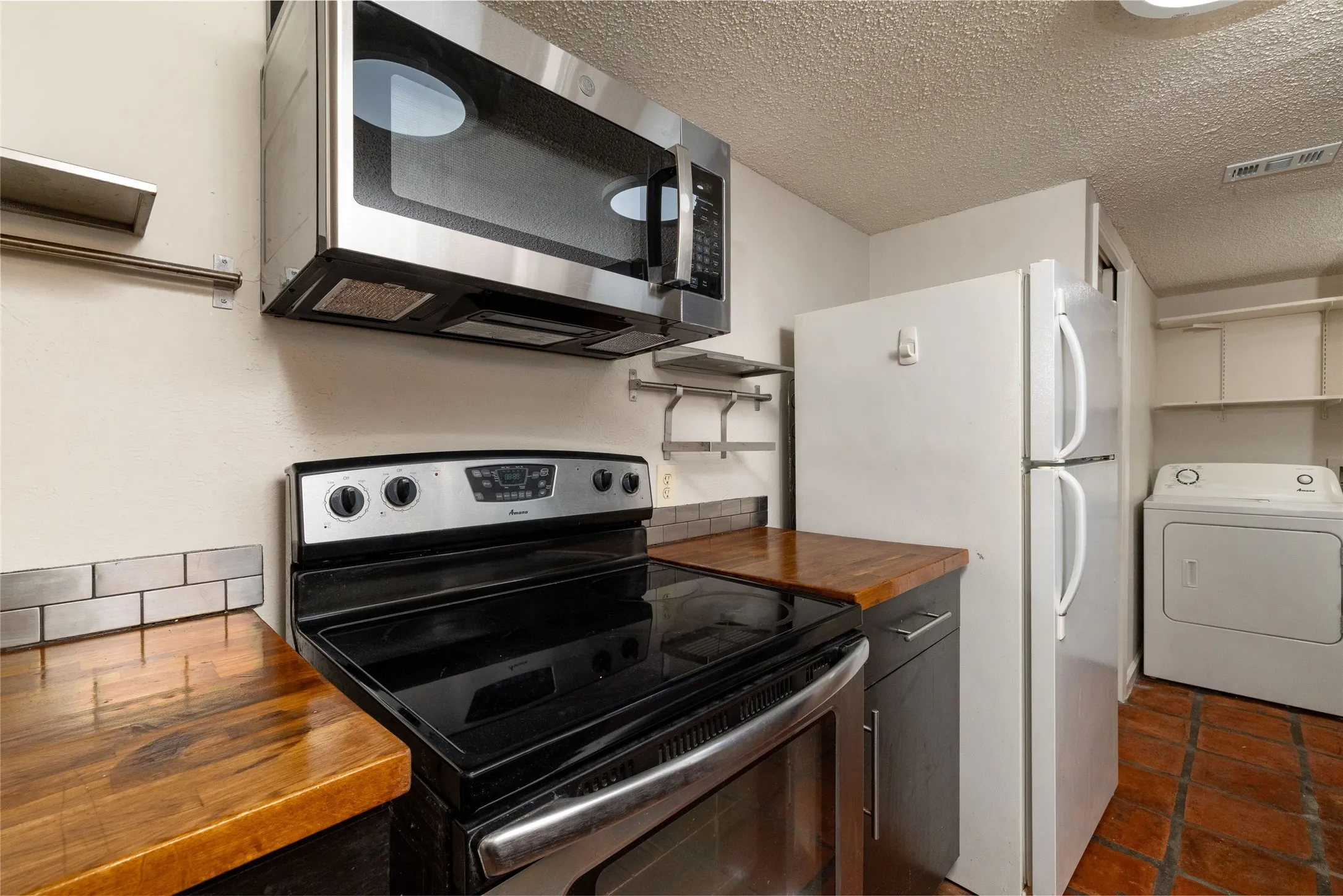 Kitchen featuring wood-finish countertops, subway tile backsplash, and stainless steel microwave