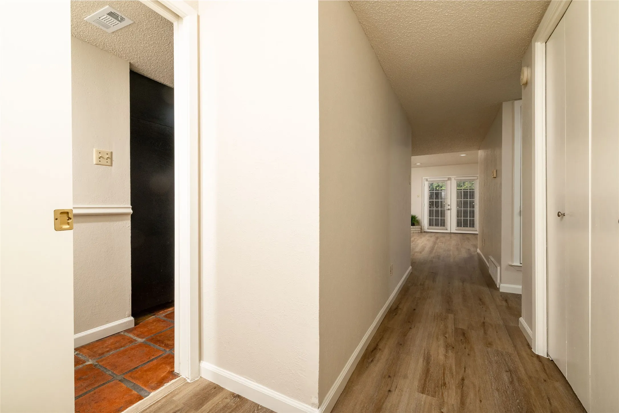 Hallway featuring wood-finish flooring, light neutral paint, white baseboards, and double French doors with grid-patterned glass