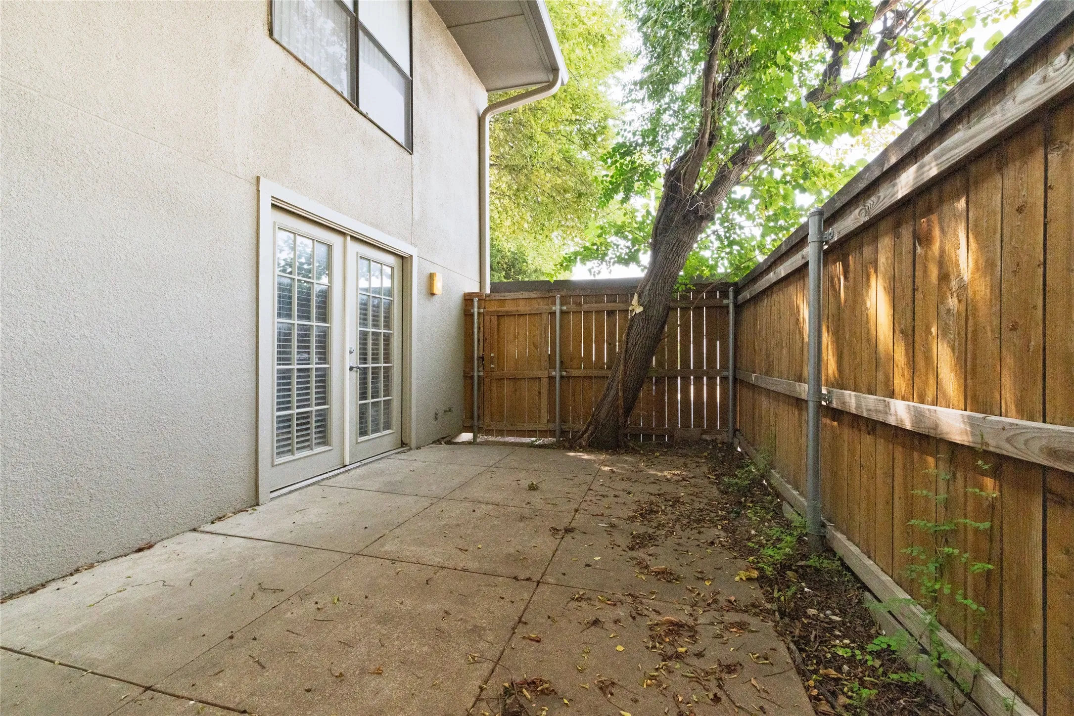 Private patio area featuring a concrete slab, stucco exterior, and double glass-paneled doors with internal blinds