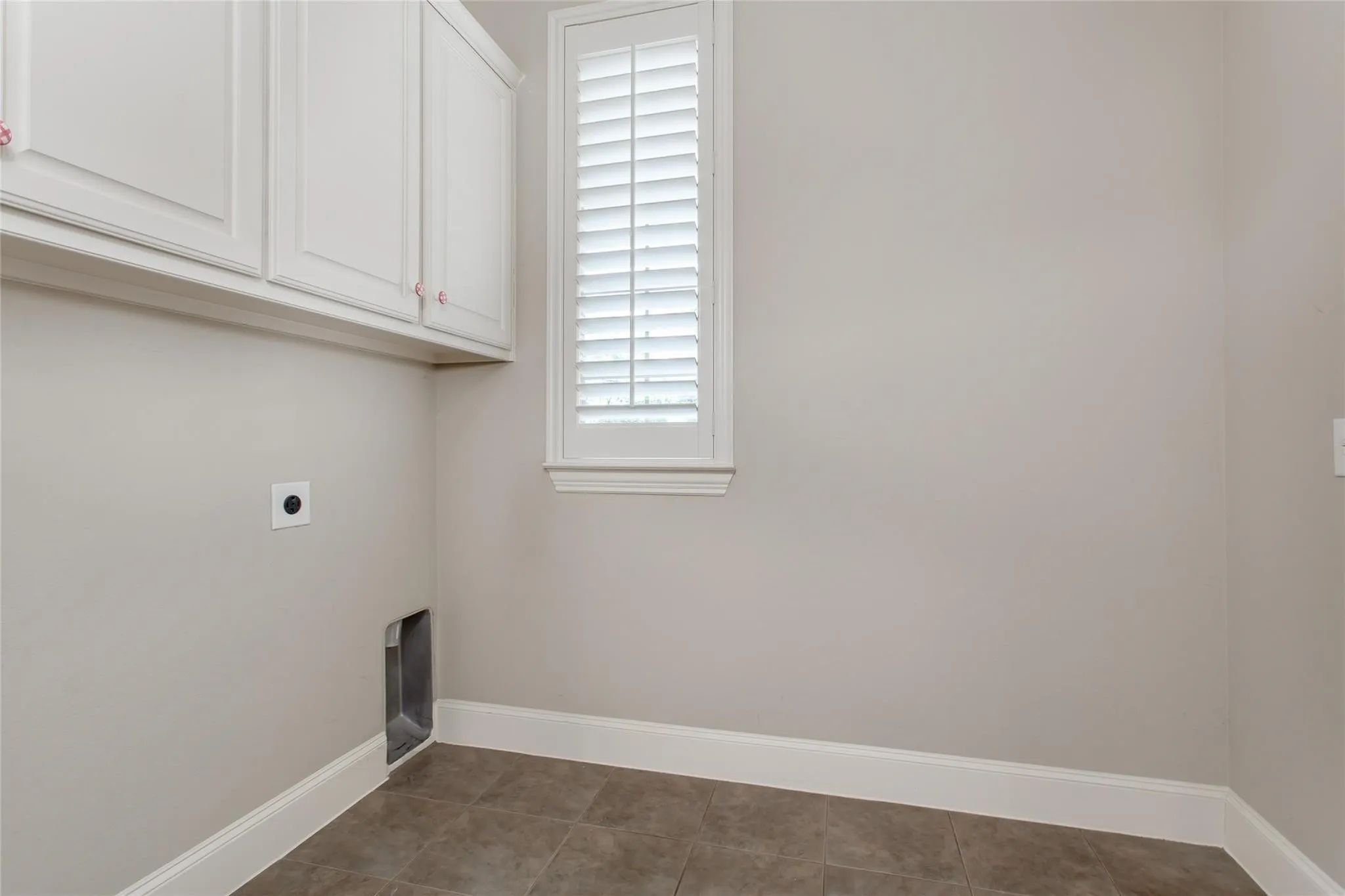 Utility area featuring white upper cabinetry, tiled flooring, a window with white louvered shutters, and light neutral wall tones