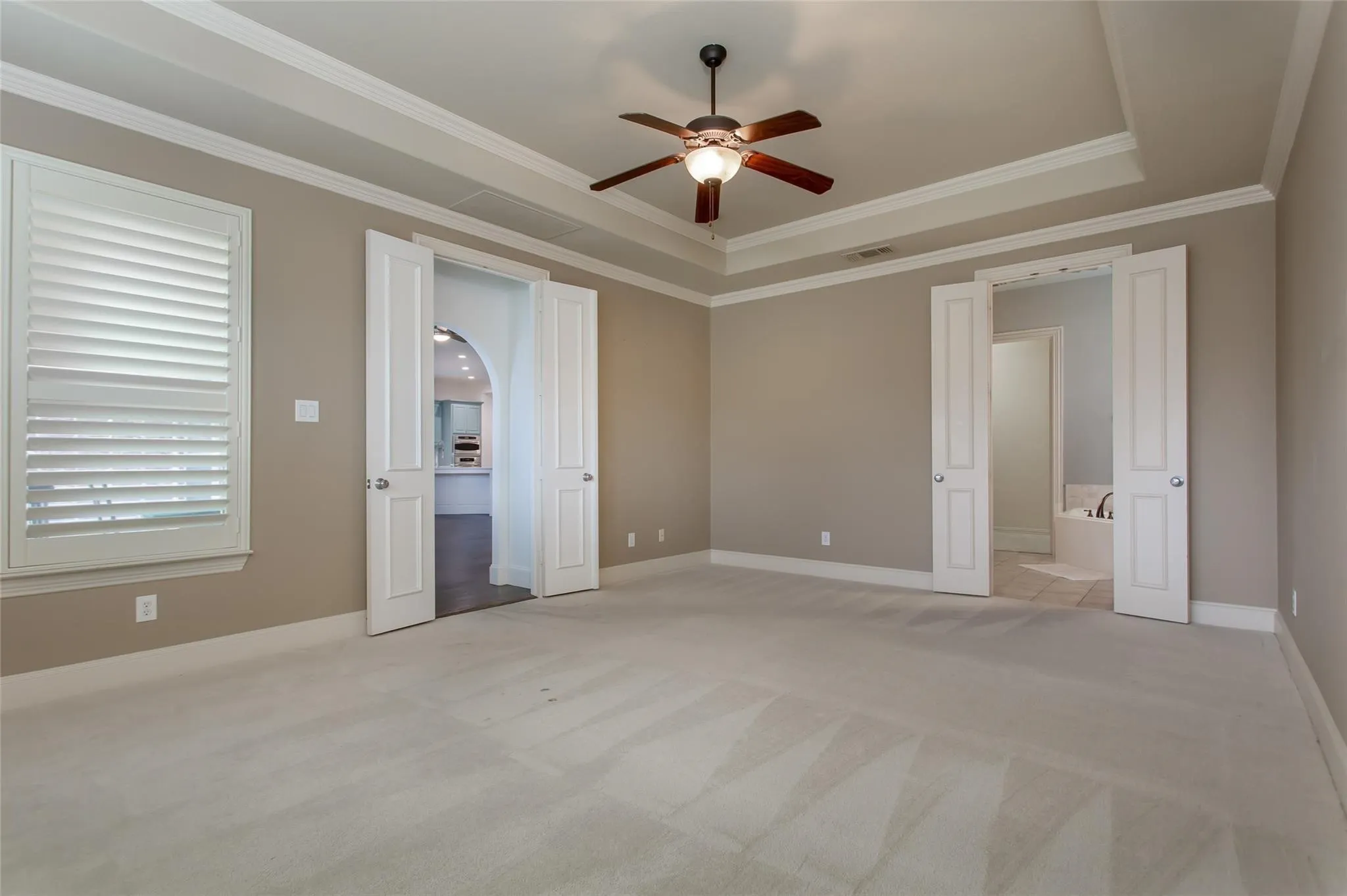 Spacious room with tray ceiling, crown molding, a ceiling fan, and carpet flooring