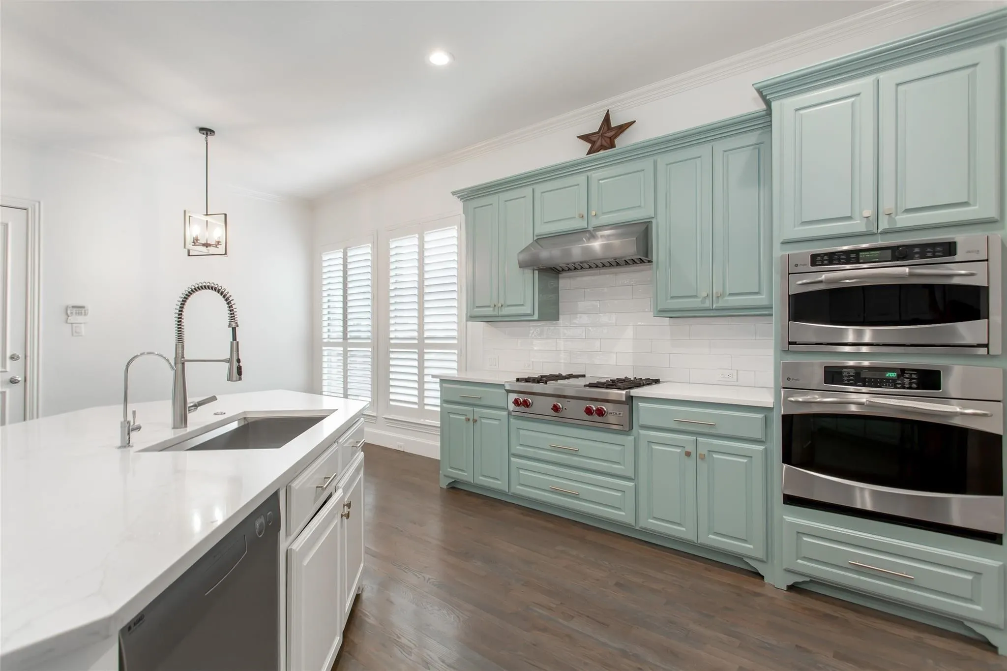Kitchen featuring light teal cabinetry, stainless steel appliances, a gas range with range hood, white subway tile backsplash, and a center island with an undermount sink and gooseneck faucet