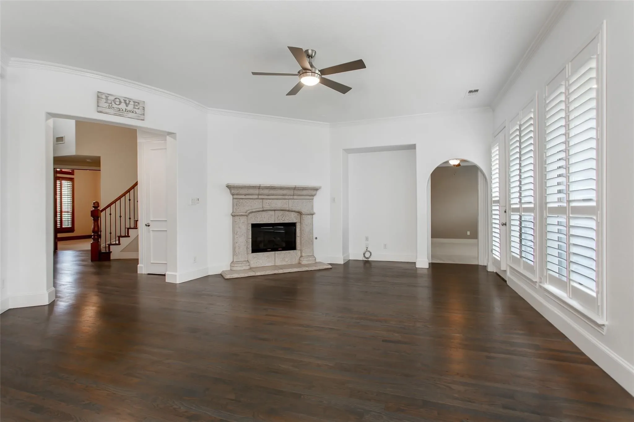 Spacious living area featuring dark wood-finish flooring, a stone-surround fireplace, and a ceiling fan