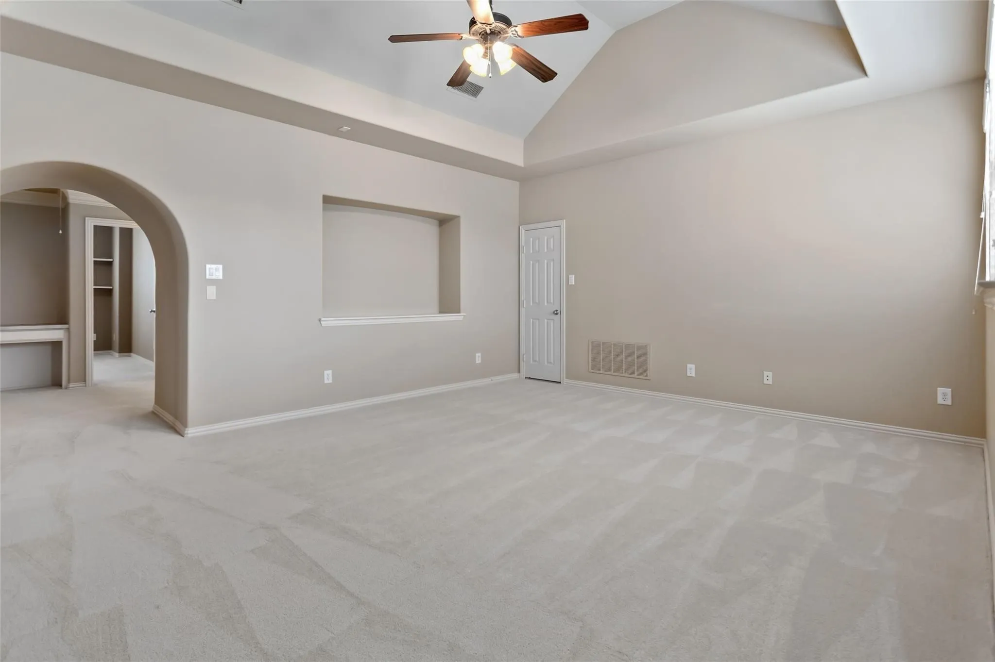 Spacious room featuring vaulted ceilings, light-toned carpeting, an arched doorway, a built-in niche, and a ceiling fan with integrated lighting