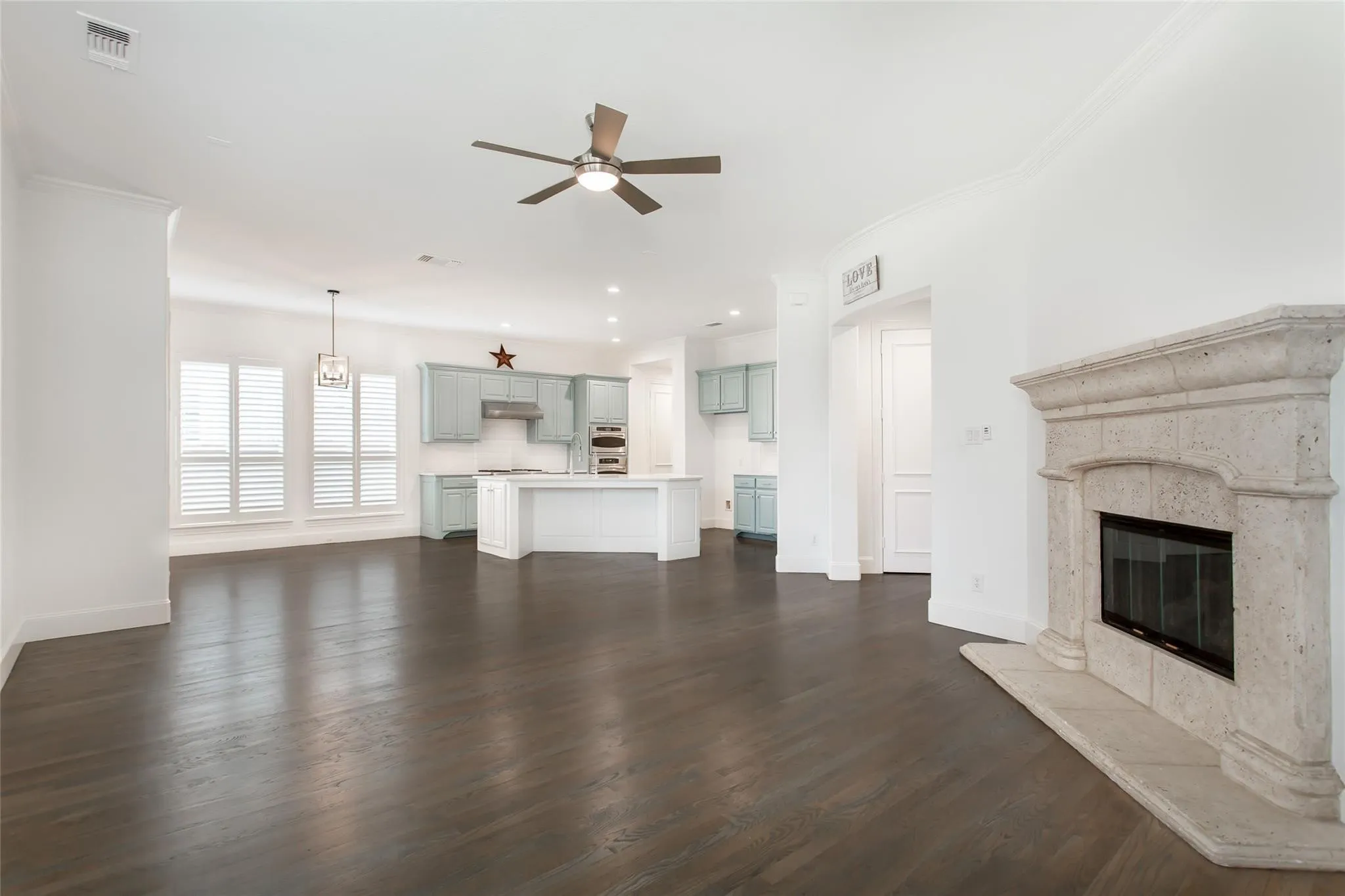 Expansive open-concept living space featuring dark wood-finish flooring, a stone fireplace, and crown molding