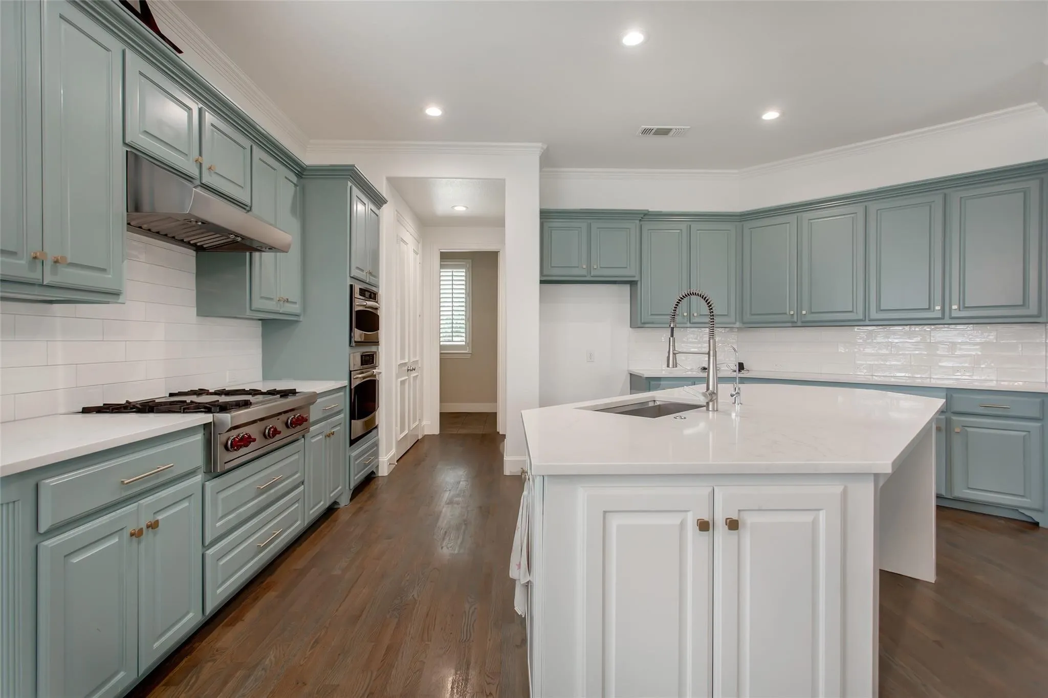 Spacious kitchen featuring light blue cabinetry, white countertops, stainless steel appliances, and a central island with an integrated sink