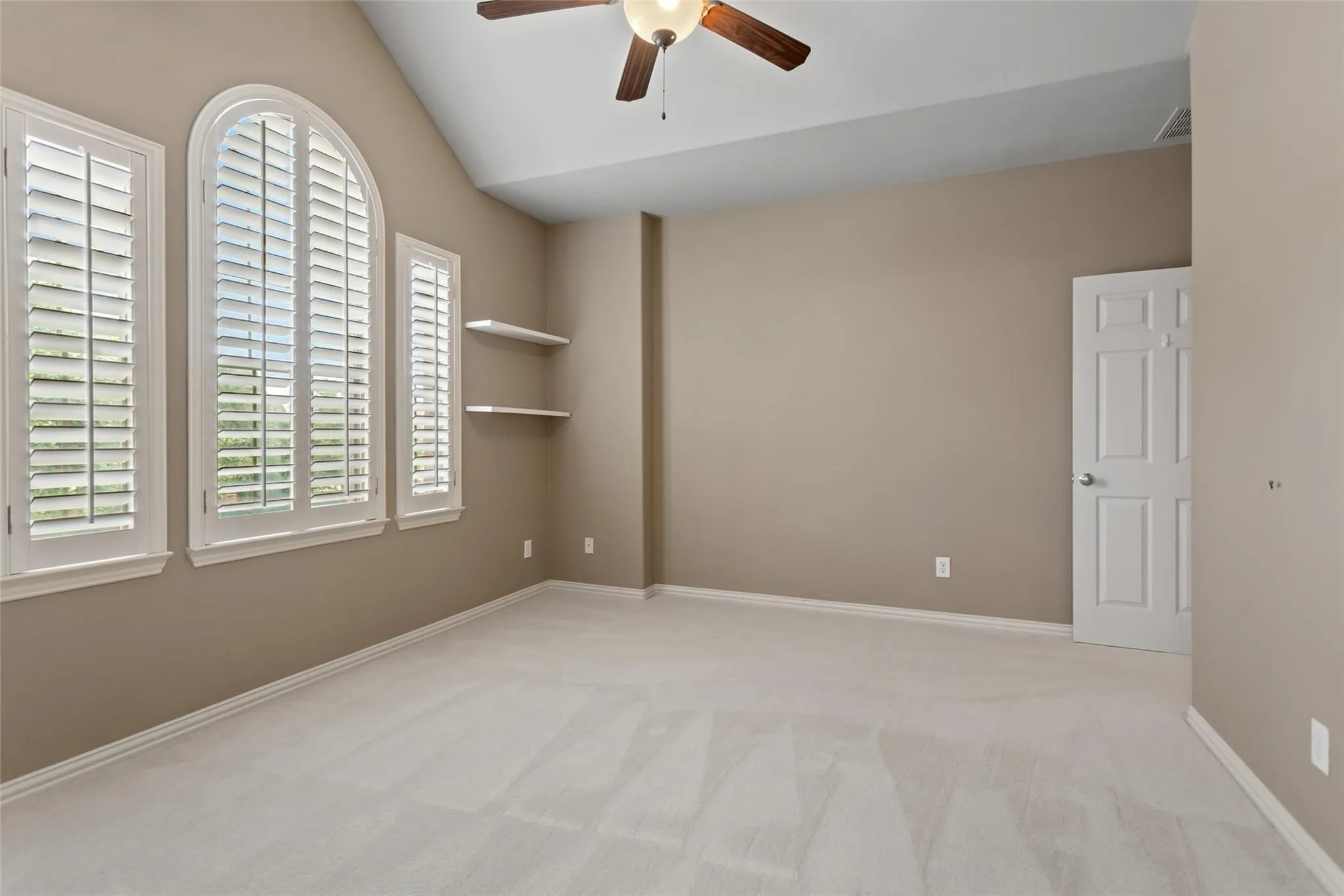 Interior room featuring an arched window flanked by two rectangular windows, all with white plantation shutters