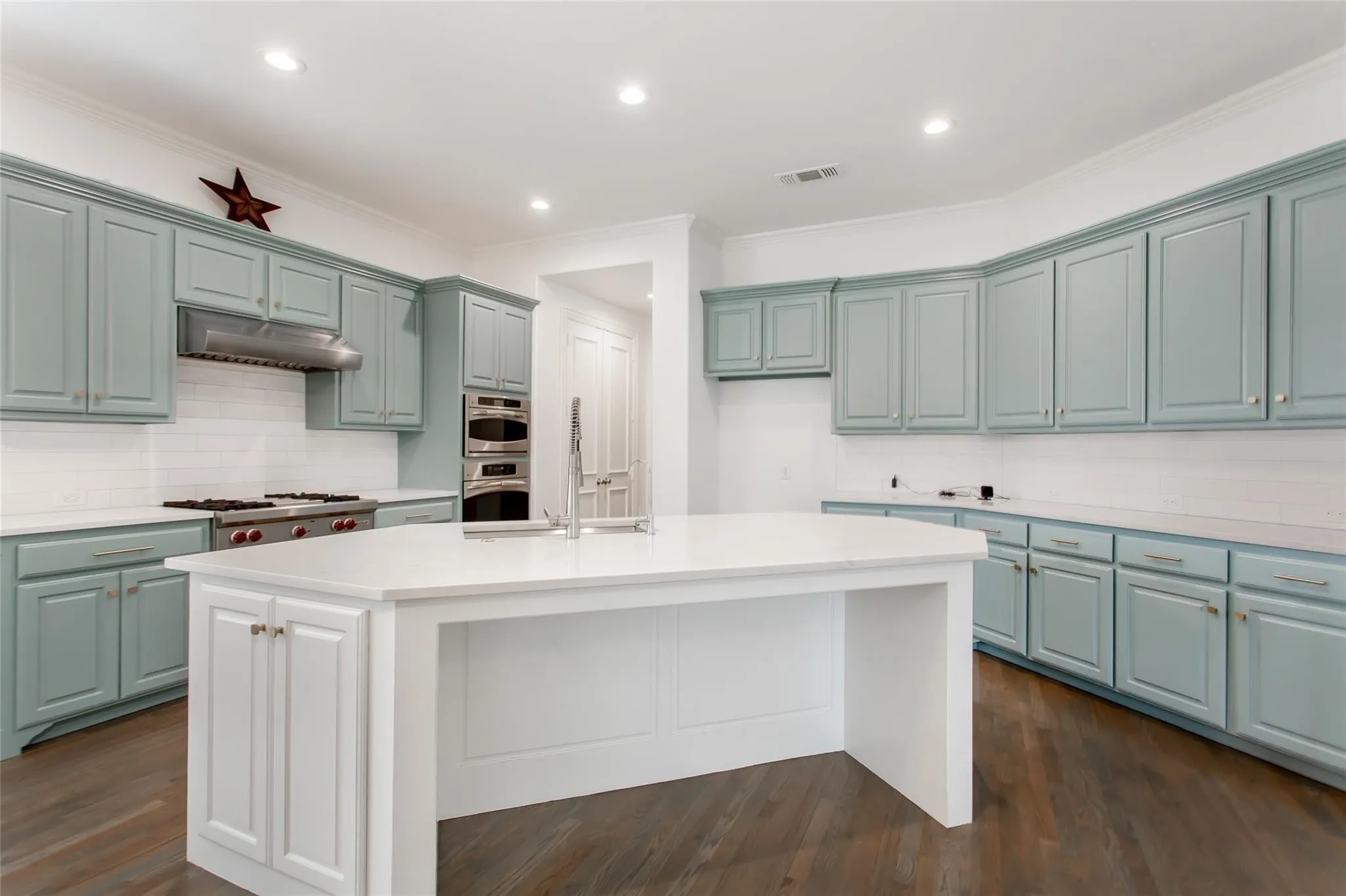 Modern kitchen featuring light blue cabinetry, a large central island with white countertops, stainless steel appliances, a subway tile backsplash, and dark wood-finish flooring