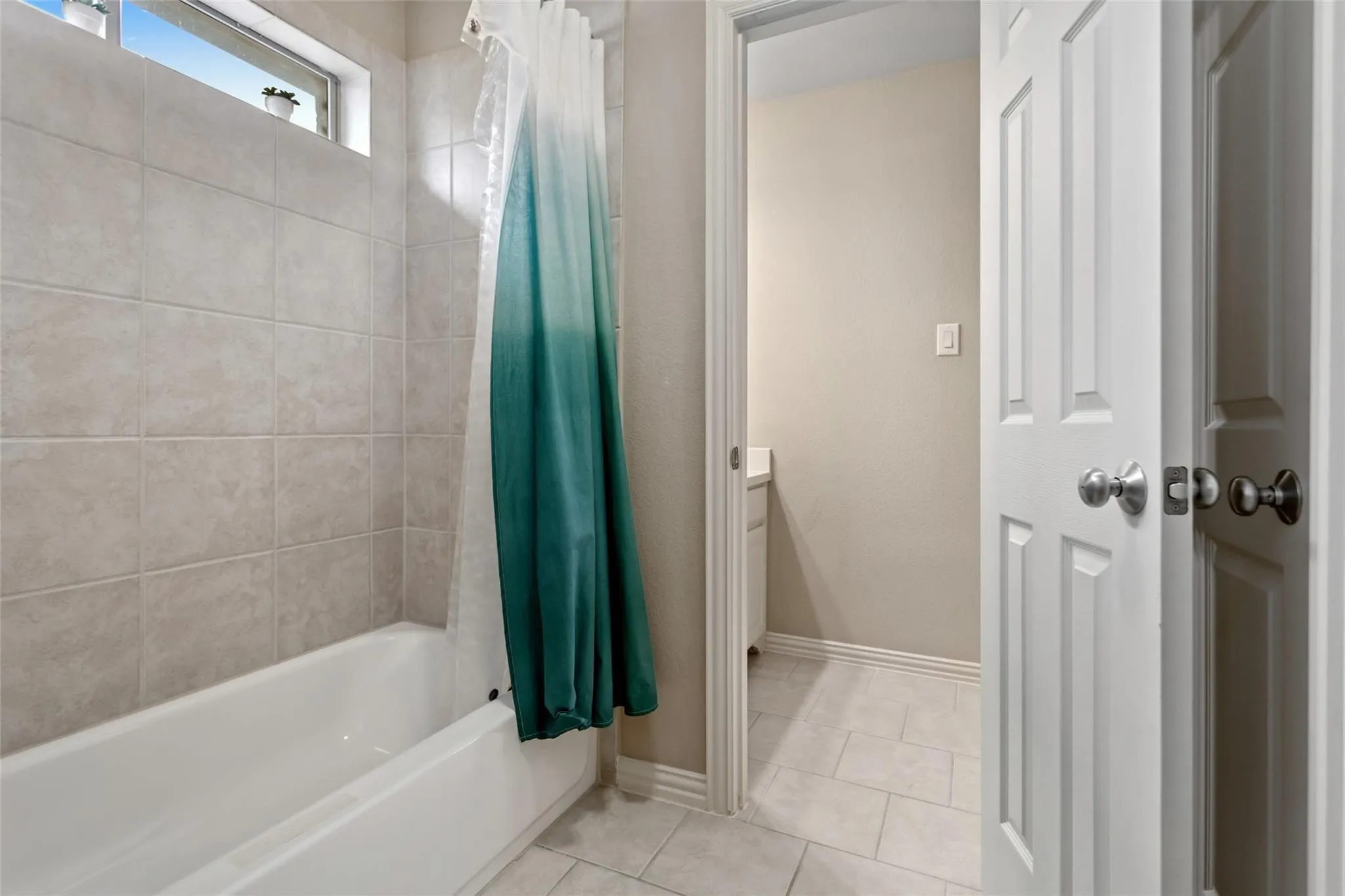 Bathroom featuring a white bathtub, light-toned tile surround, and an upper transom window