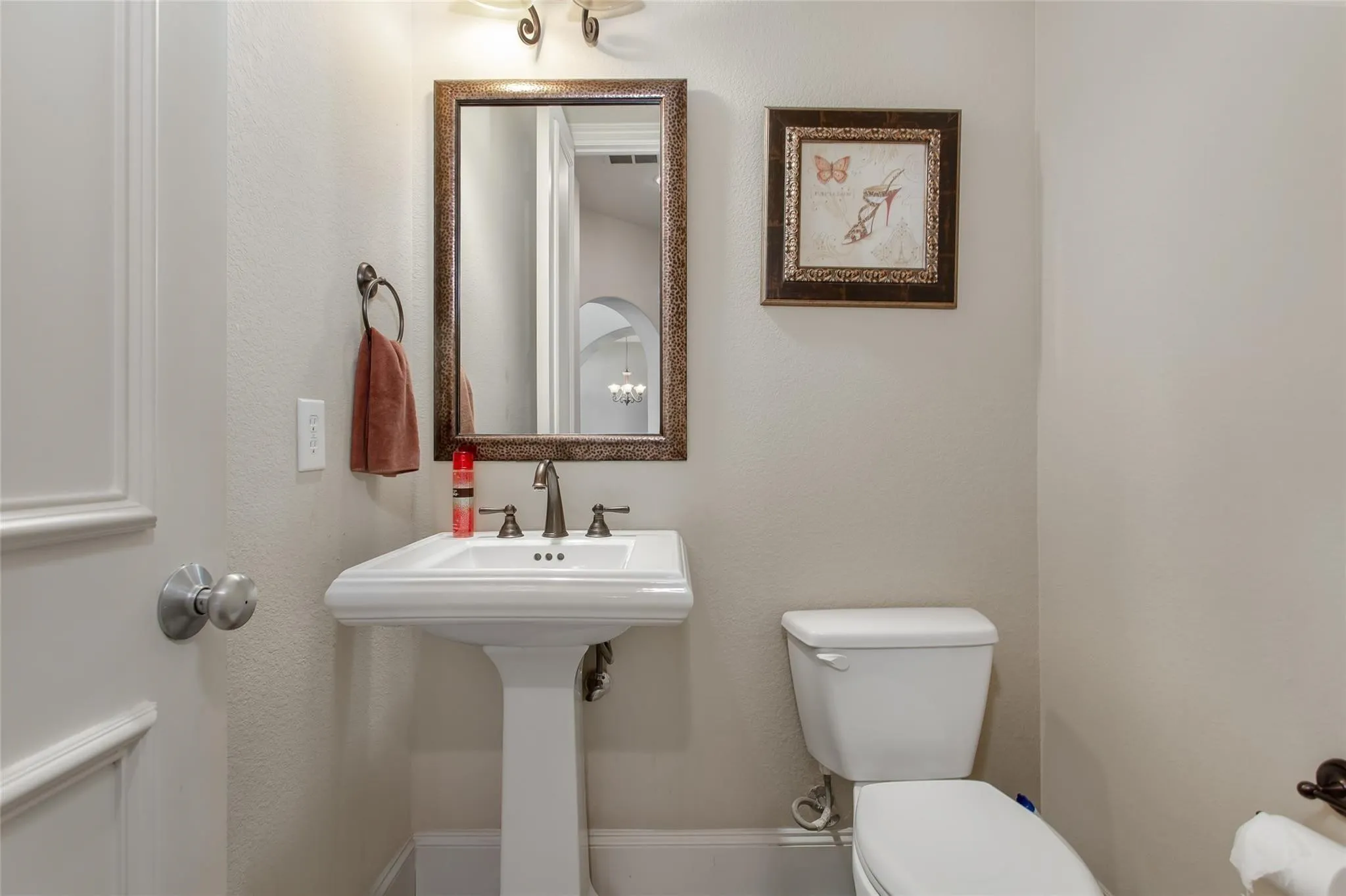 Pedestal sink with a three-piece bronze-finish faucet, framed mirror, and decorative wall sconce lighting