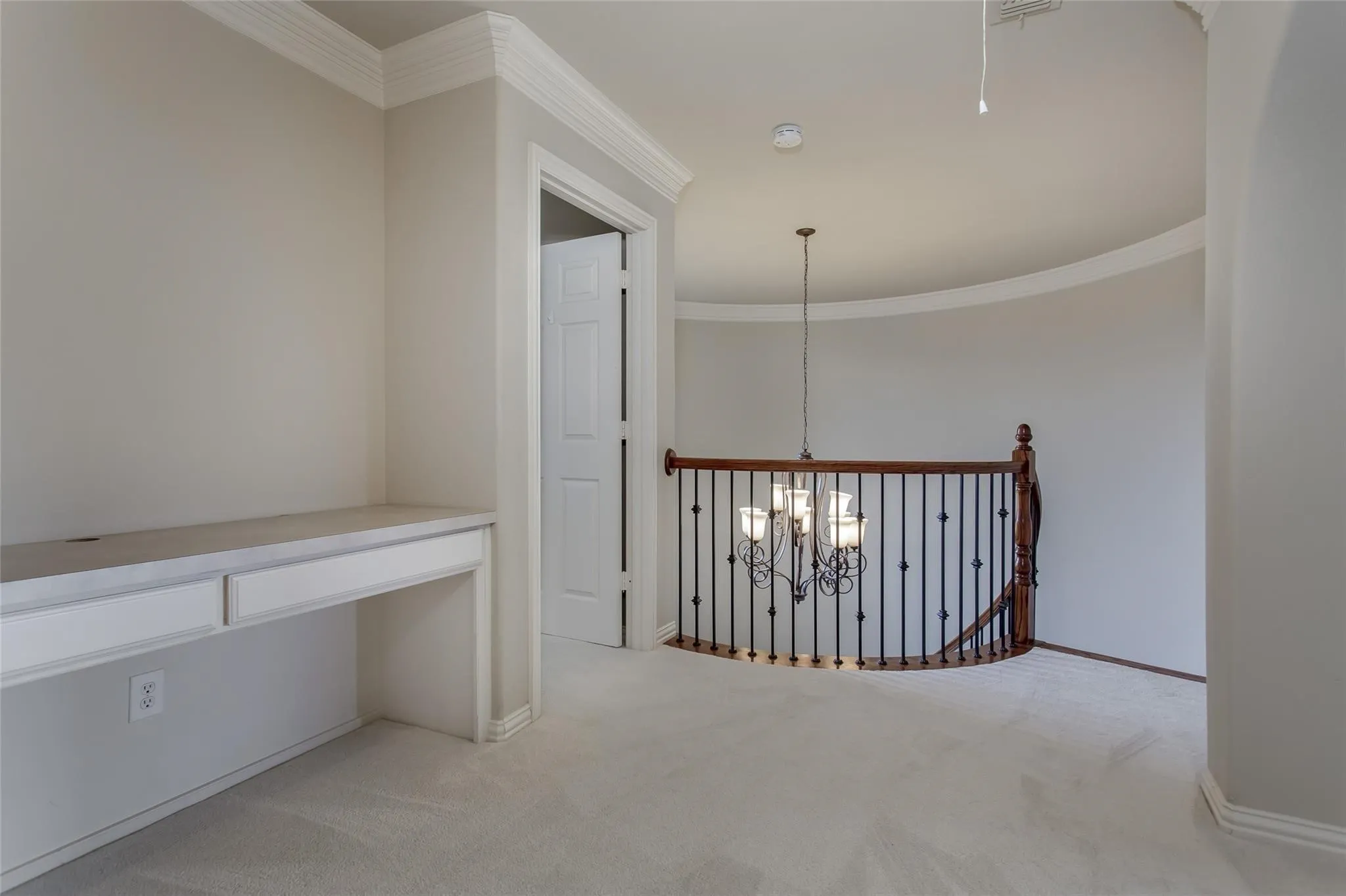 Upper-level landing featuring a built-in desk with two drawers, crown molding, and a curved staircase with wood newel posts and iron balusters