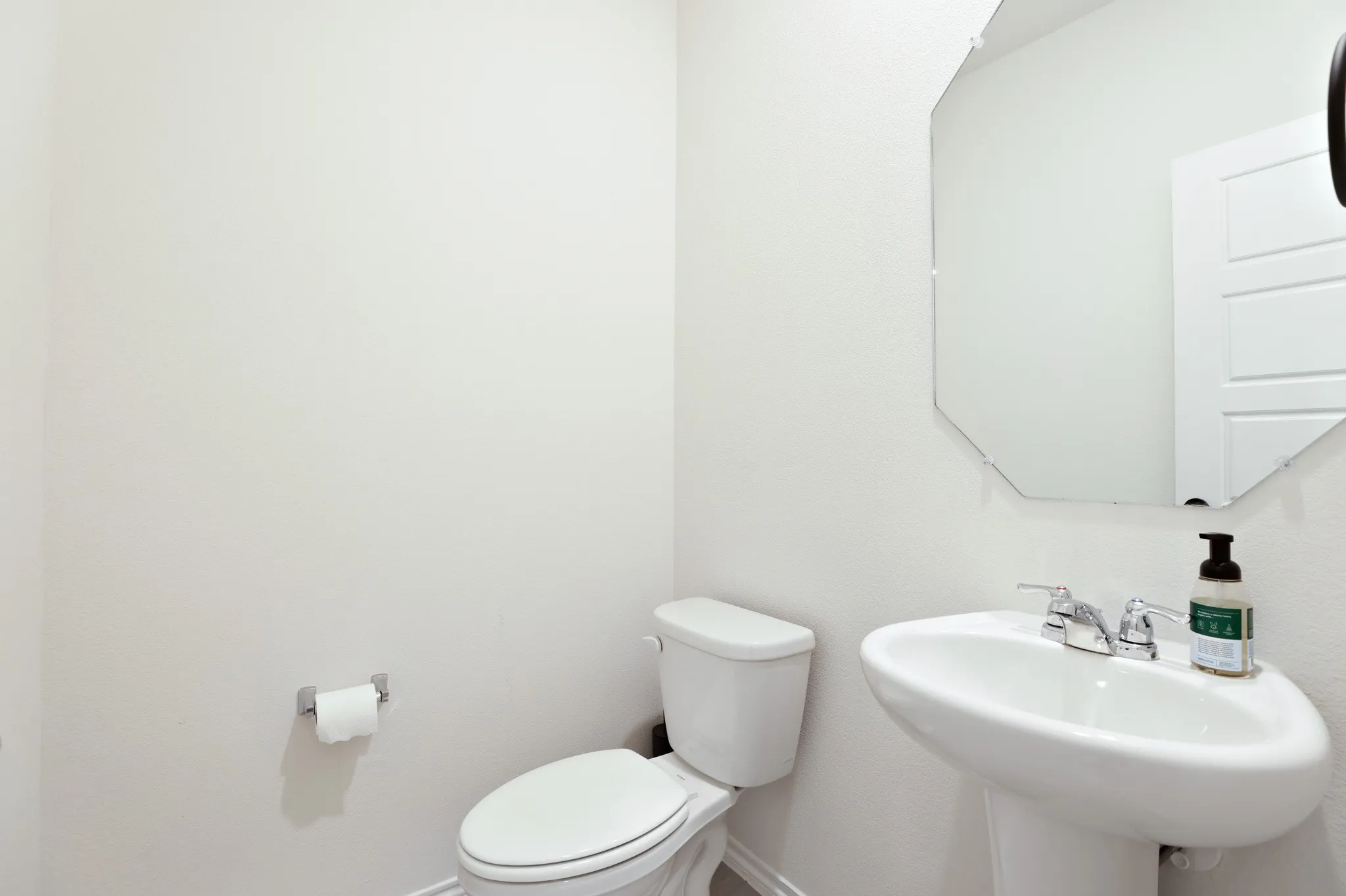 White pedestal sink with chrome faucet and an octagonal mirror