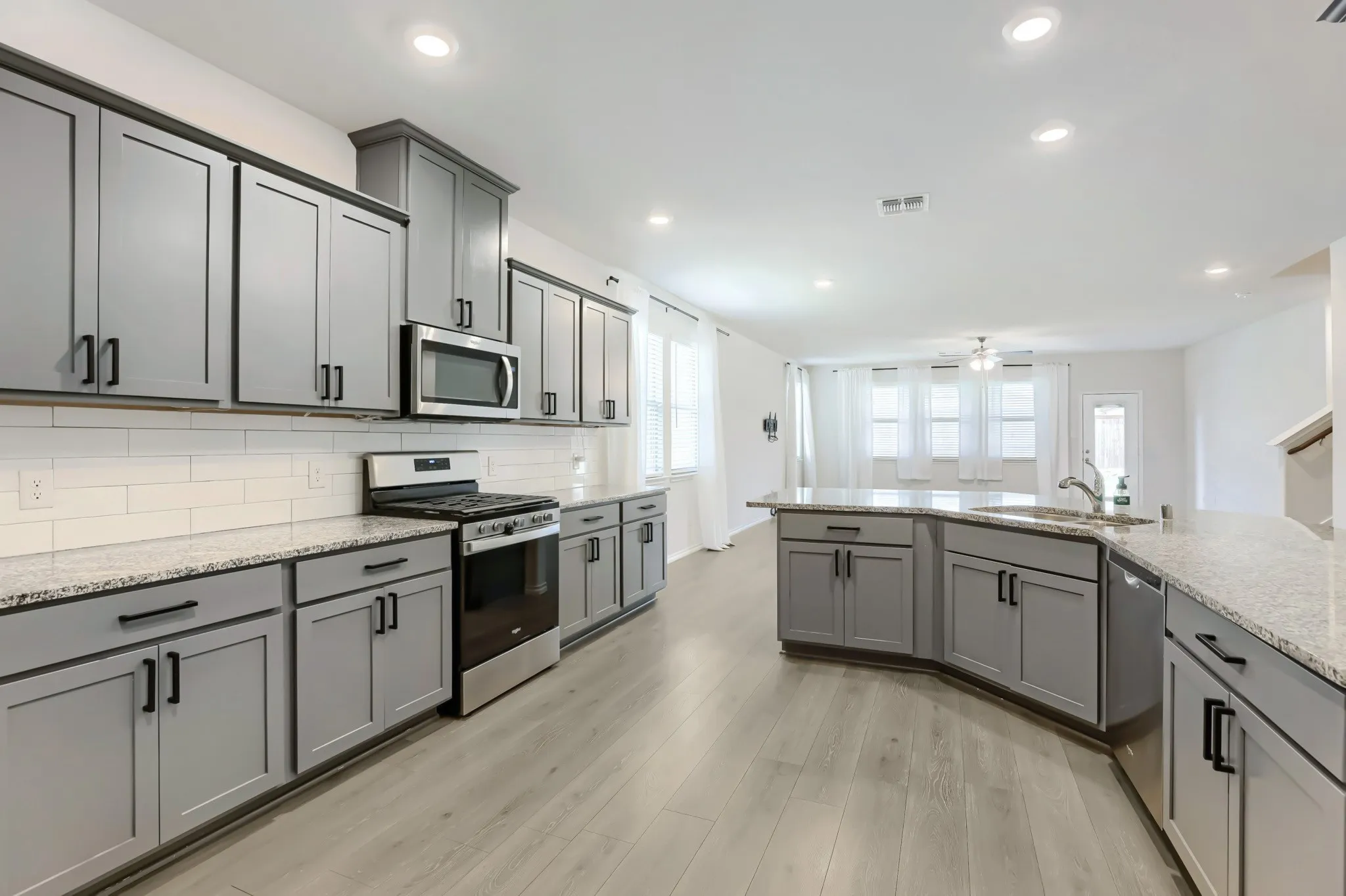 Kitchen featuring gray cabinetry with black hardware, white subway tile backsplash, stainless steel appliances, wood-finish flooring, and recessed lighting