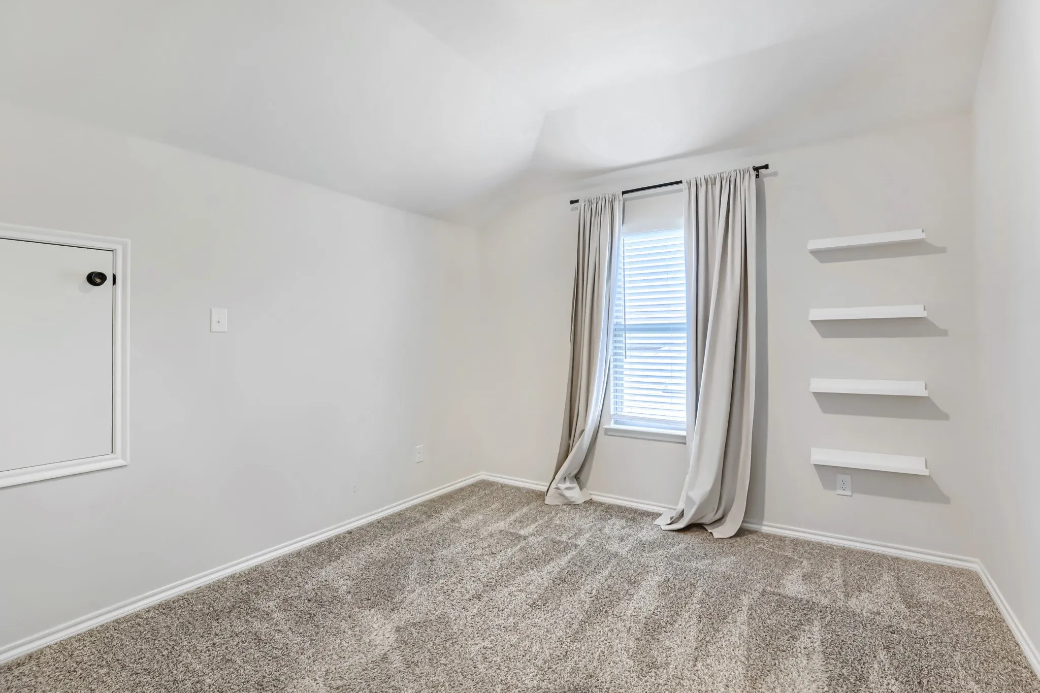 Textured carpeting, window with horizontal blinds, and four wall-mounted floating shelves