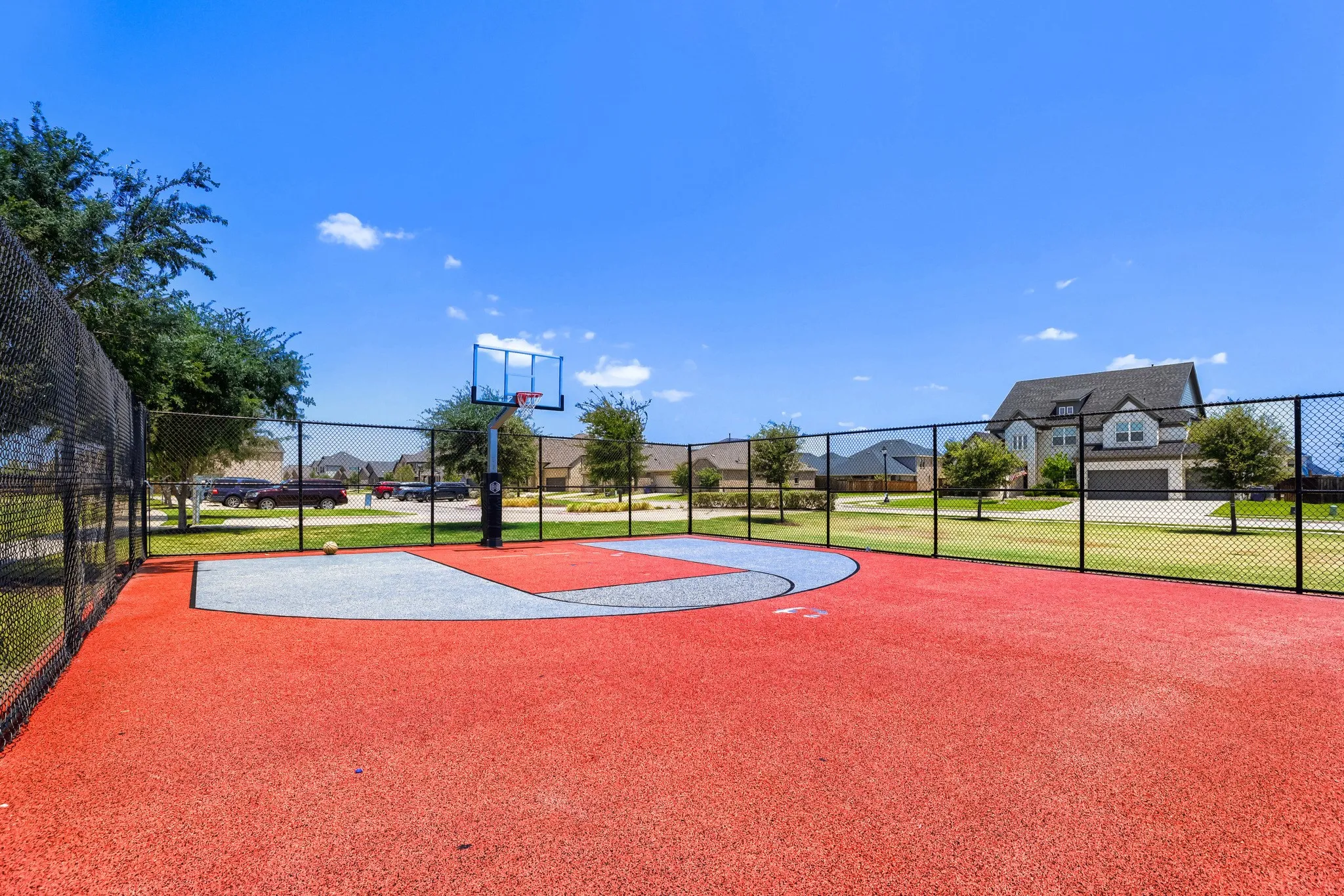 Fenced court with a basketball hoop, featuring a red and gray surface