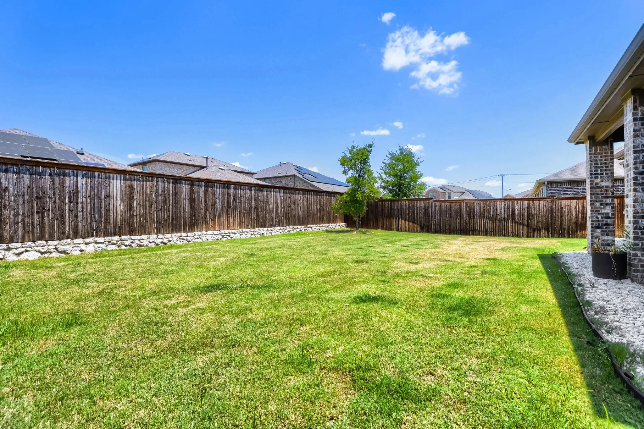Expansive grass lawn bordered by a tall privacy fence and a decorative stone retaining wall